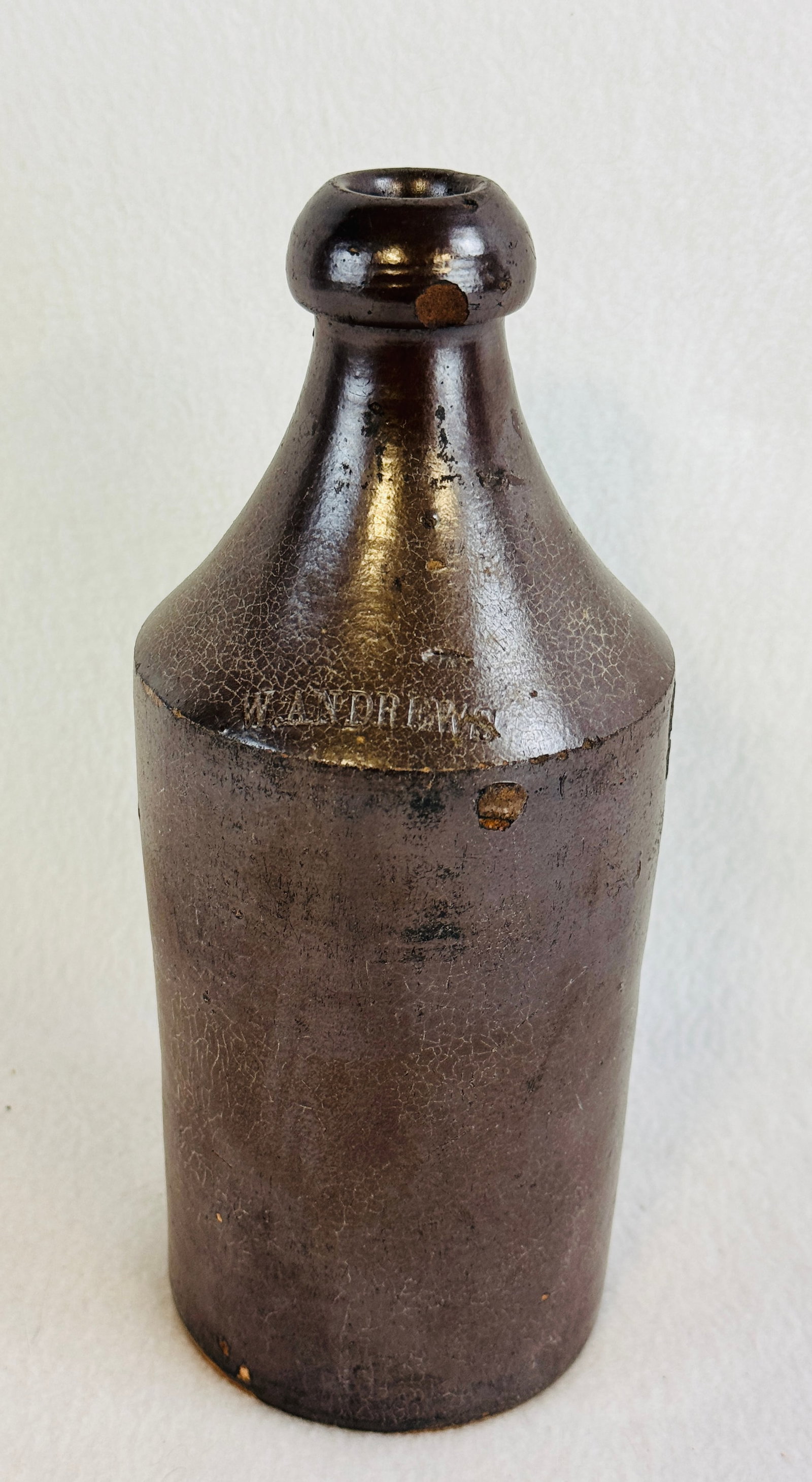 Pottery Bottle W Andrews: 9" Albany slip glazed pottery bottle (hard to tell if its redware or stoneware made with a lot of local clay included) which is impressed at shoulder W. Andrews. Condition - small chip to top blob lip