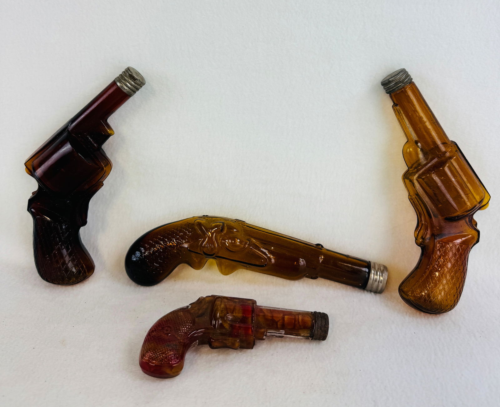 Lot 4 Pistol Form Figural Bottles: Lot of four antique figural bottles in the form of pistols three of which are of amber glass with ground mouths and having their original nickel plated brass screw on caps. The last and smallest bottl