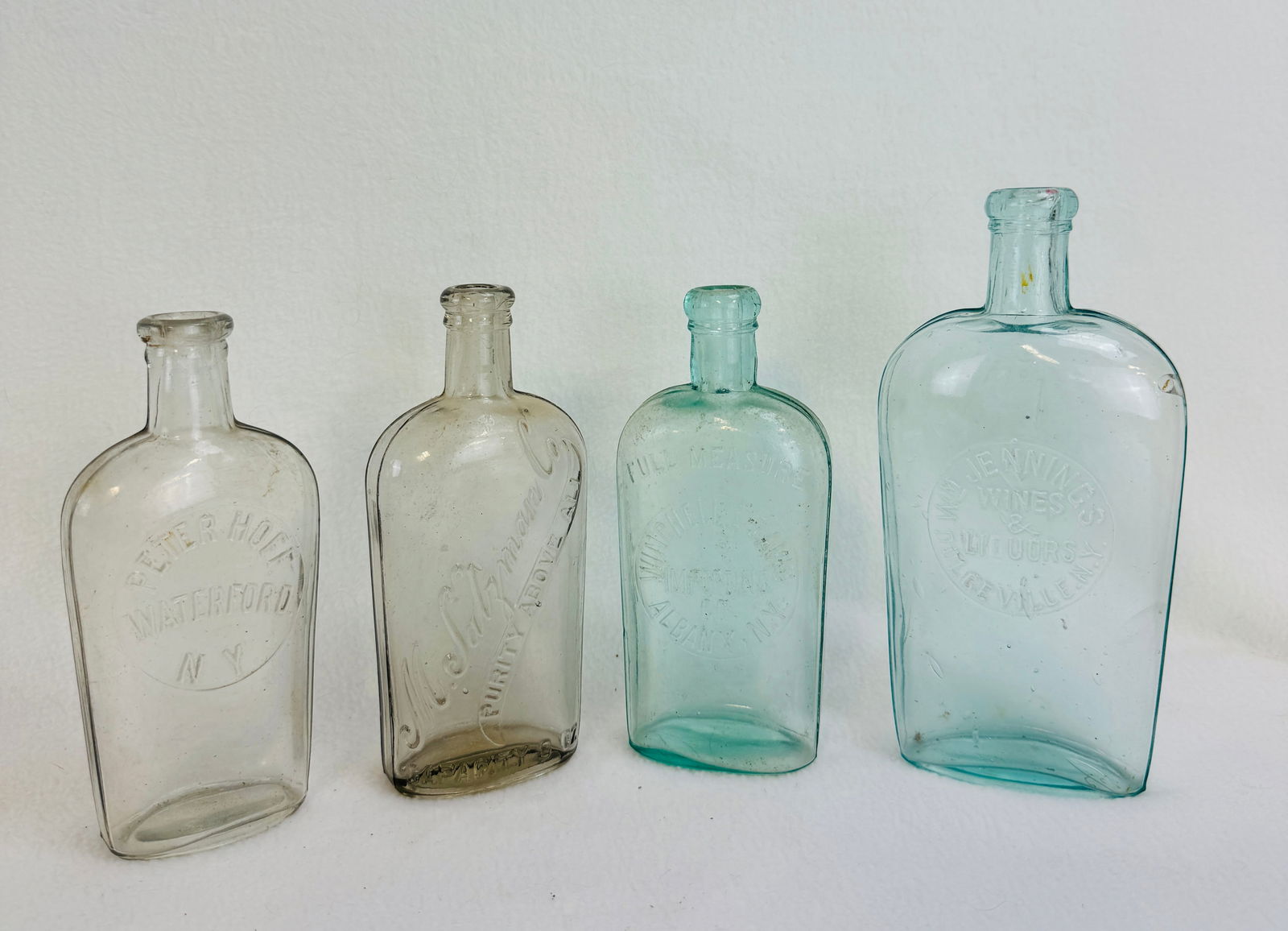 Lot 4 Embossed Strap Sided Whiskey Flasks: Lot of four embossed strap sided whiskey flasks to include: clear half pint M. Salzman Co, aquamarine Winchell & Davis Albany NY, clear Peter Hoff Waterford N.Y., and finally a aquamarine Wm Jennings