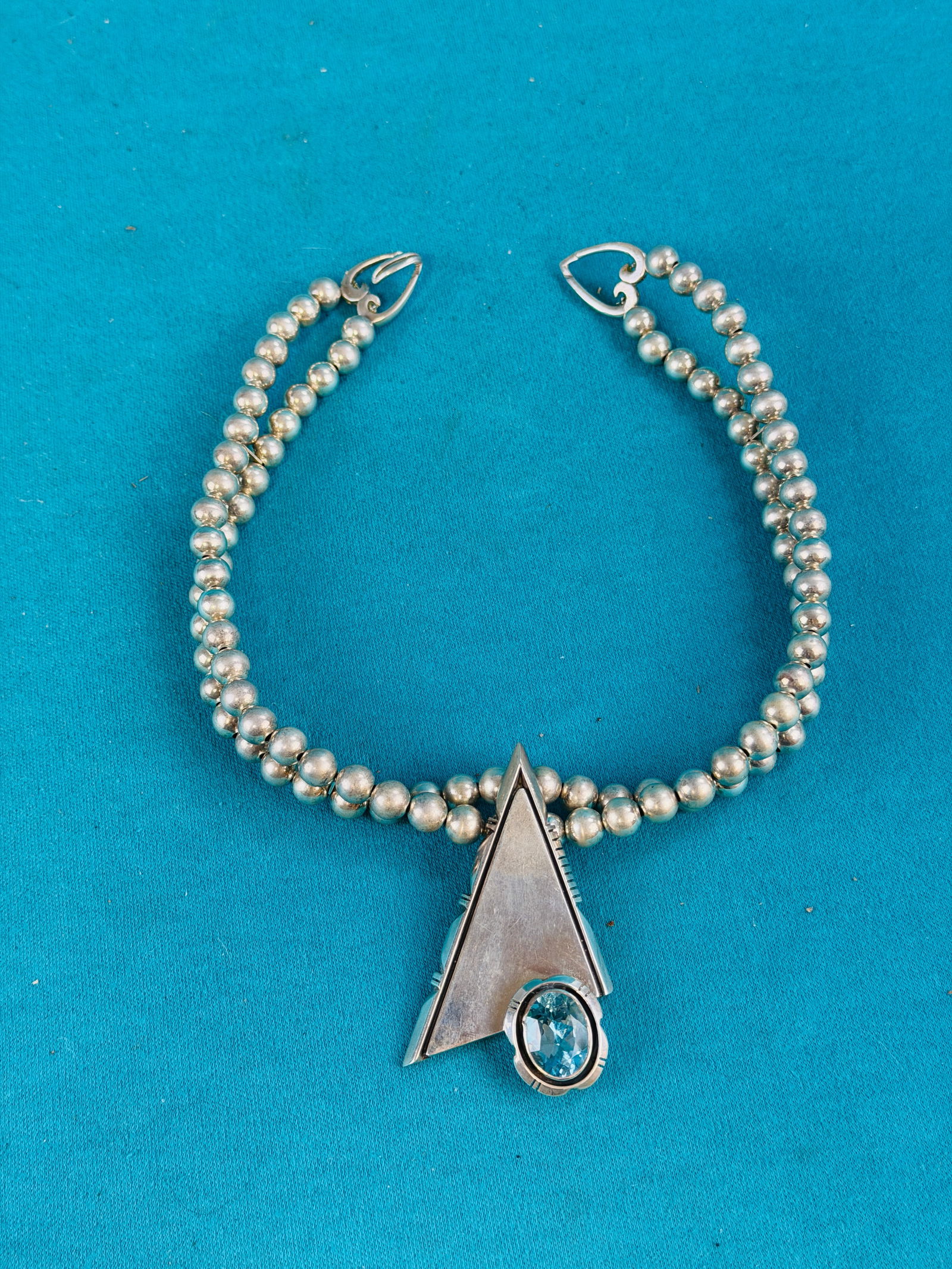 Modernist Sterling Necklace: Modernism marked sterling silver necklace which is titled by artist "SUNRISE" with heart form clasps and a triangular pendant set with a blue faceted stone. Necklace is in excellent condition. The wei