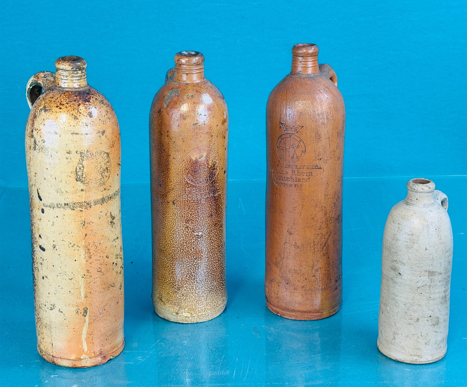 Lot 4 European Ginger Beer Bottles: Lot of four European stoneware handled ginger beer bottles of which three measure approximately 11 1/2" tall and one 7". The three larger specimens are debossed with retailers name etc while the small
