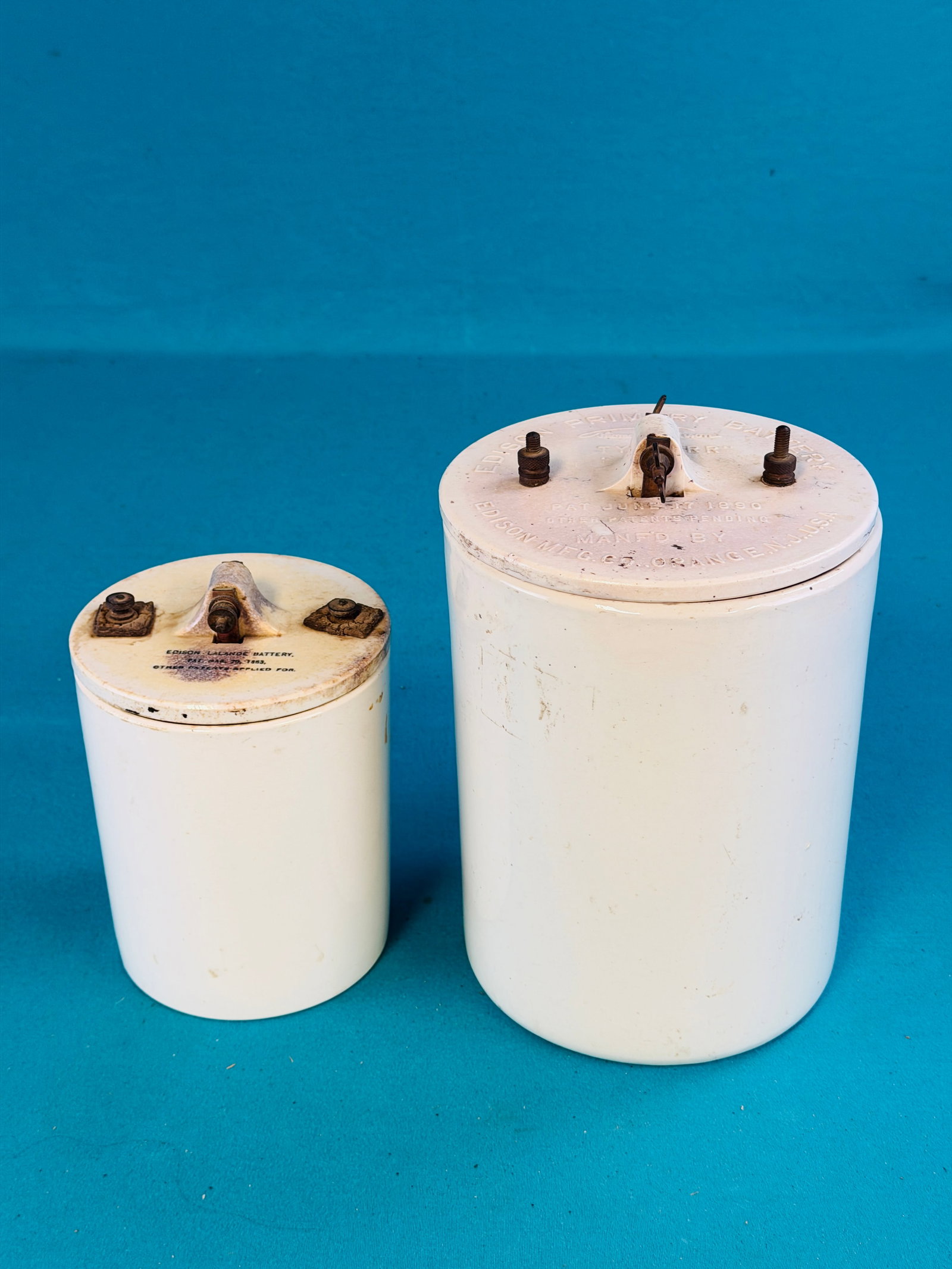 Lot 2 Edison Ceramic Battery Jars: Lot of two different sizes of white ceramic Edison battery jars with electrodes. The taller jar measures approximately 10 1/4" tall. Condition - smaller jar has some chipping to the glaze on the inter