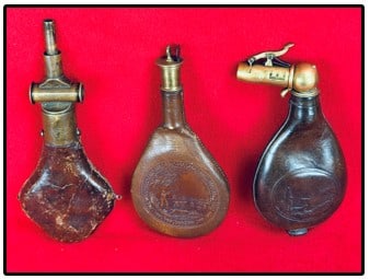Lot 3 Leather Shot Flasks With Unusual Brass Chargers: Lot of three leather shot flasks each equipped with a unusual brass charger. Two of the flasks have embossed hunting scenes showing a hunter with rifle and hunting dog in a woodland setting while the 