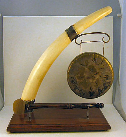 Ivory tusk mounted brass gong, late 19th or early 2: Ivory tusk mounted brass gong, late 19th or early 20th century, plated metal mounts, base measures 14" X 8.75", gong 7", ivory tusk 21.25" long measured on outer curve