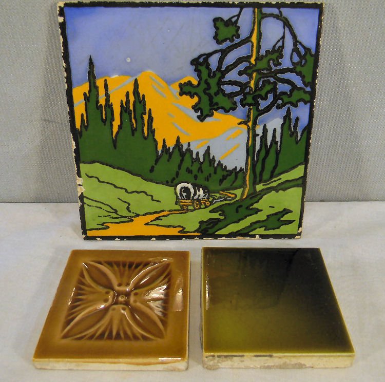 Tiles including Dec. Art scenic tile of covered w: Tiles including Dec. Art scenic tile of covered wagon traveling along mountainside, 6" square flakes on edges and ding in sky, together with two 3" majolica square tiles, on marked Low.