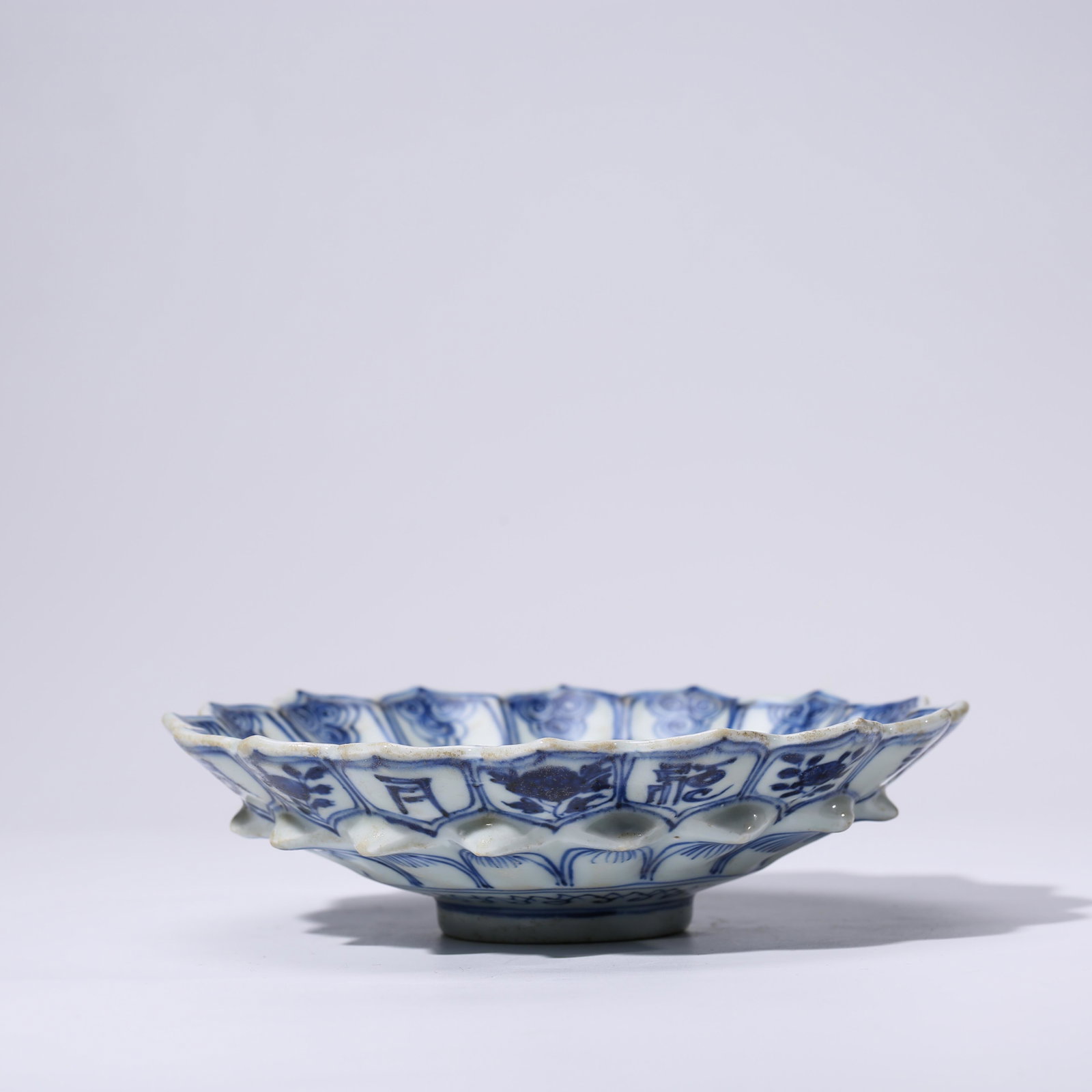 A CHINESE BLUE & WHITE PORCELAIN FU DISH MARKED WAN LI: Dimensions: Diam.18.8cm, Height: 5.2cm, The dish is of shallow form with rounded sides divided into six lobes on the interior by ribs of slip that rise to the everted rim surrounding a central floral 