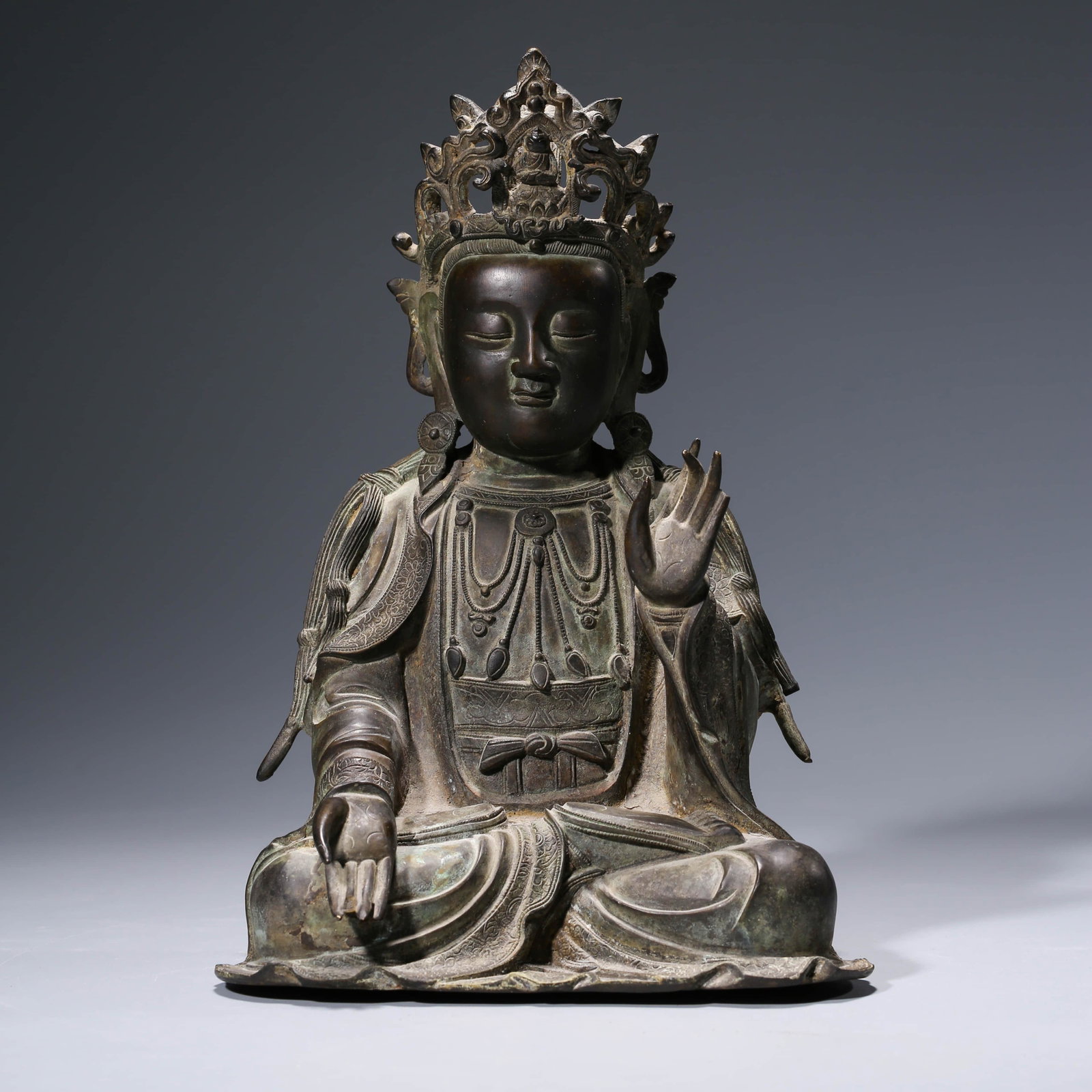 A CHINESE BRONZE AVALOKITESHVARA STATUE: Dimensions: Weight: 4860g Length: 20.3cm, Width: 10.1cm, Height: 29.5cm, Seated with one hand in the air and the otheron the lap, wearing voluminous robes falling in elegant folds from his shoulders, 