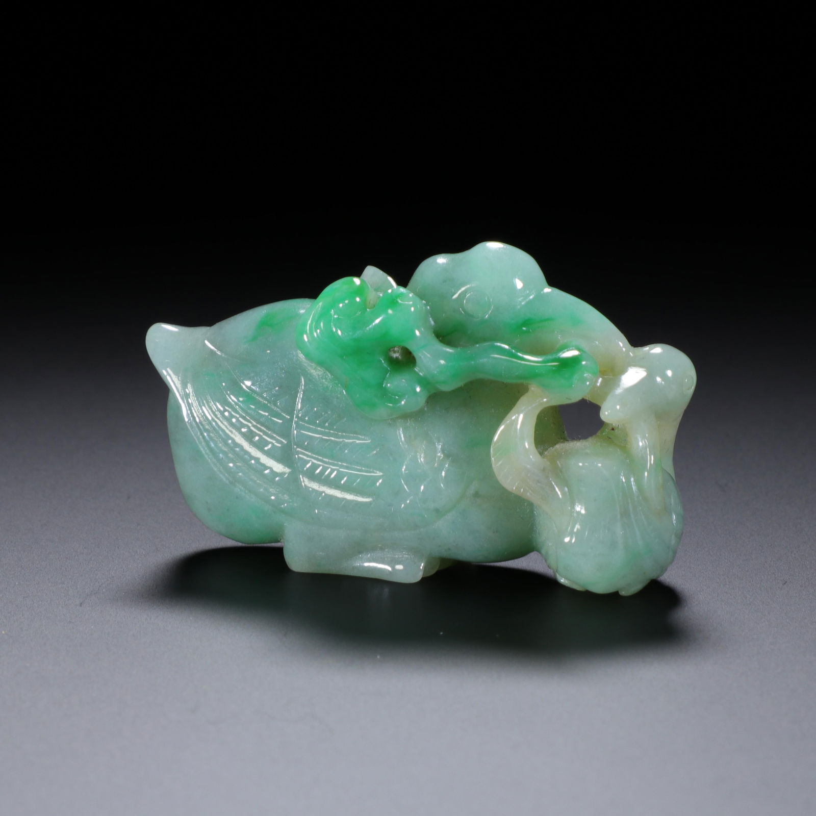 CHINESE JADEITE GOOSE WITH GANODERMA: Dimensions: H. 2.7 cm. W. 4.5 cm. This petite Chinese jadeite carving depicts a goose holding a ganoderma fungus, measuring 2.7 cm in height and 4.5 cm in width, crafted from celadon jadeite with vibr