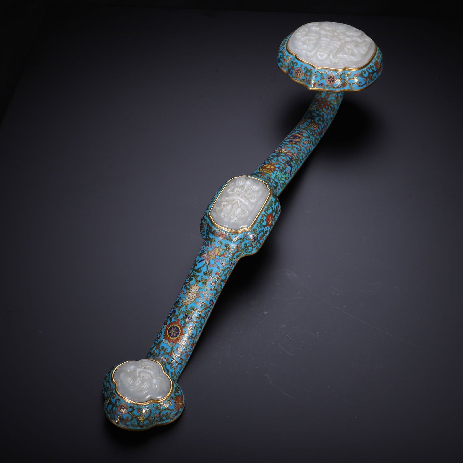 CHINESE CLOISONN? RUYI WITH WHITE JADE INLAY: Dimensions: L. 47 cm. This exquisite Chinese cloisonn? Ruyi scepter features vibrant turquoise enamel grounds adorned with intricate filigree scrollwork, masterfully accented with gilt-bronze borders.