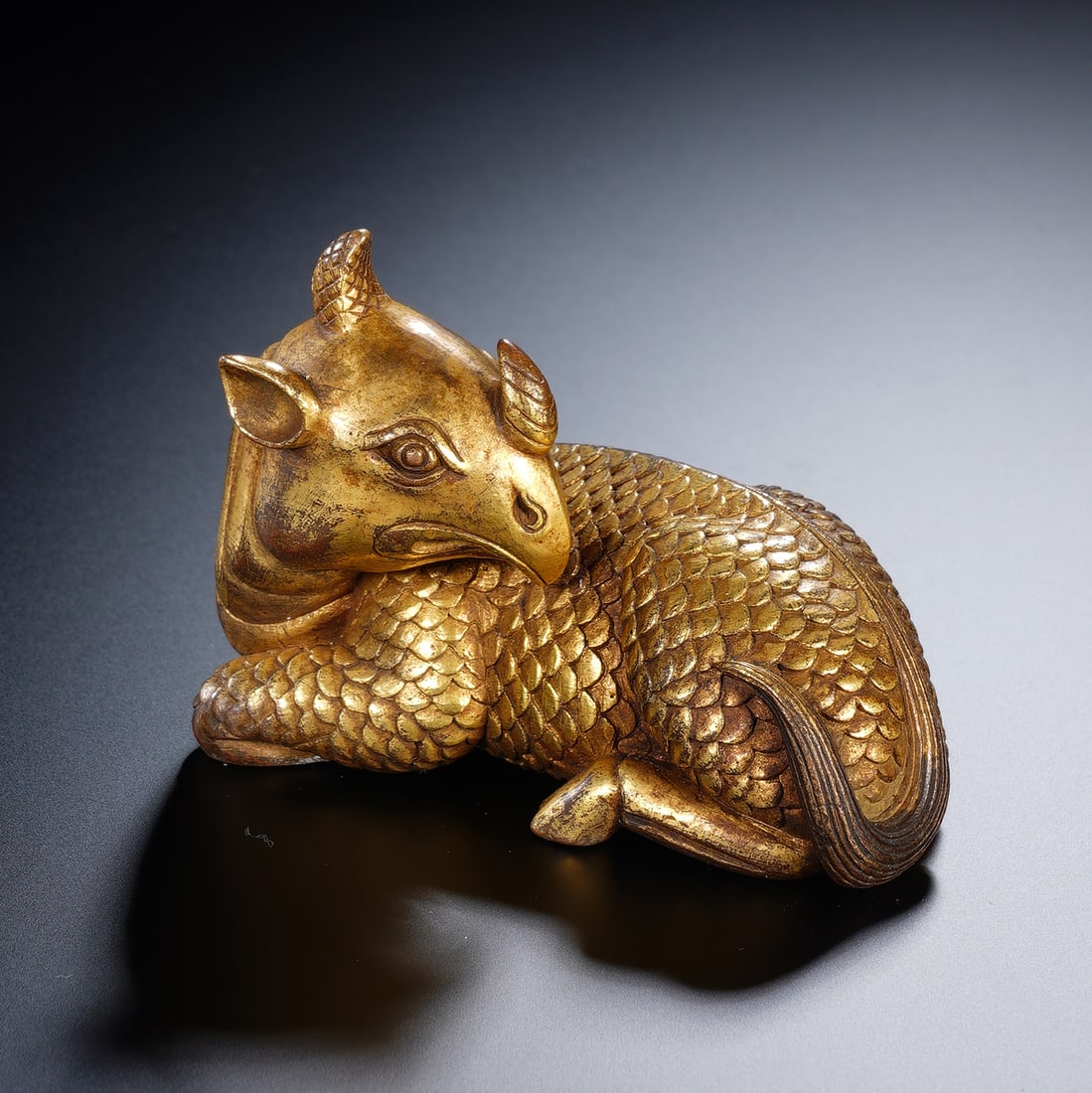 CHINESE GILT BRONZE AUSPICIOUS BEAST WEIGHT: Dimensions: 8x4x6 cm. Weight 596 grams. This Chinese gilt bronze paper weight is modeled as a recumbent mythical ruishou (auspicious beast) with a unicorn horn, scaled body, and bird-like beak,