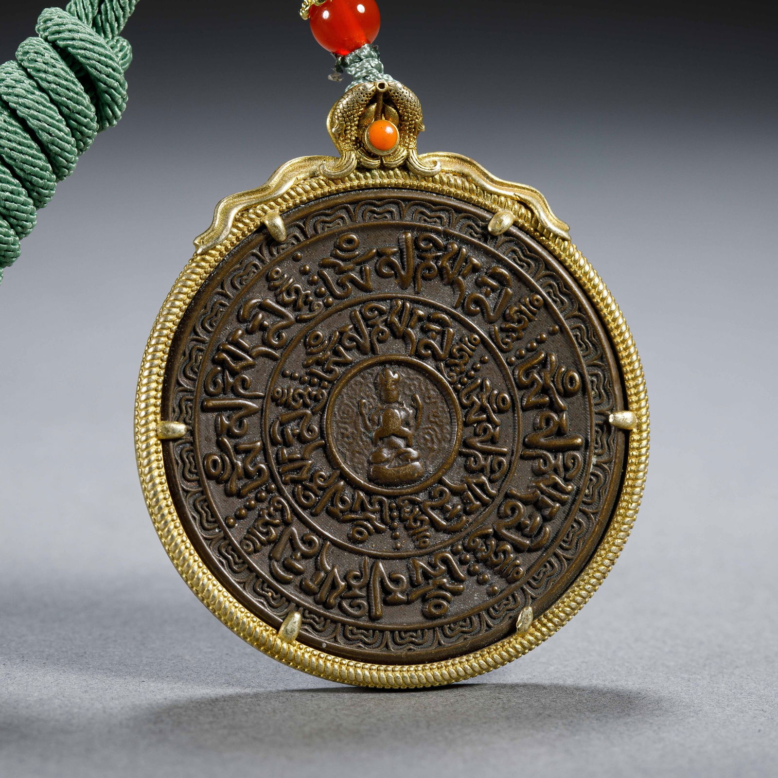 CHINESE GILT BRONZE NINE PALACE PENDANT: Dimensions: L. 4.6 cm. H. 5.4 cm. Weight 50 grams. This Chinese gilt bronze Nine Palace pendant features a circular form with intricate Tibetan script and Buddhist motifs carved in relief,