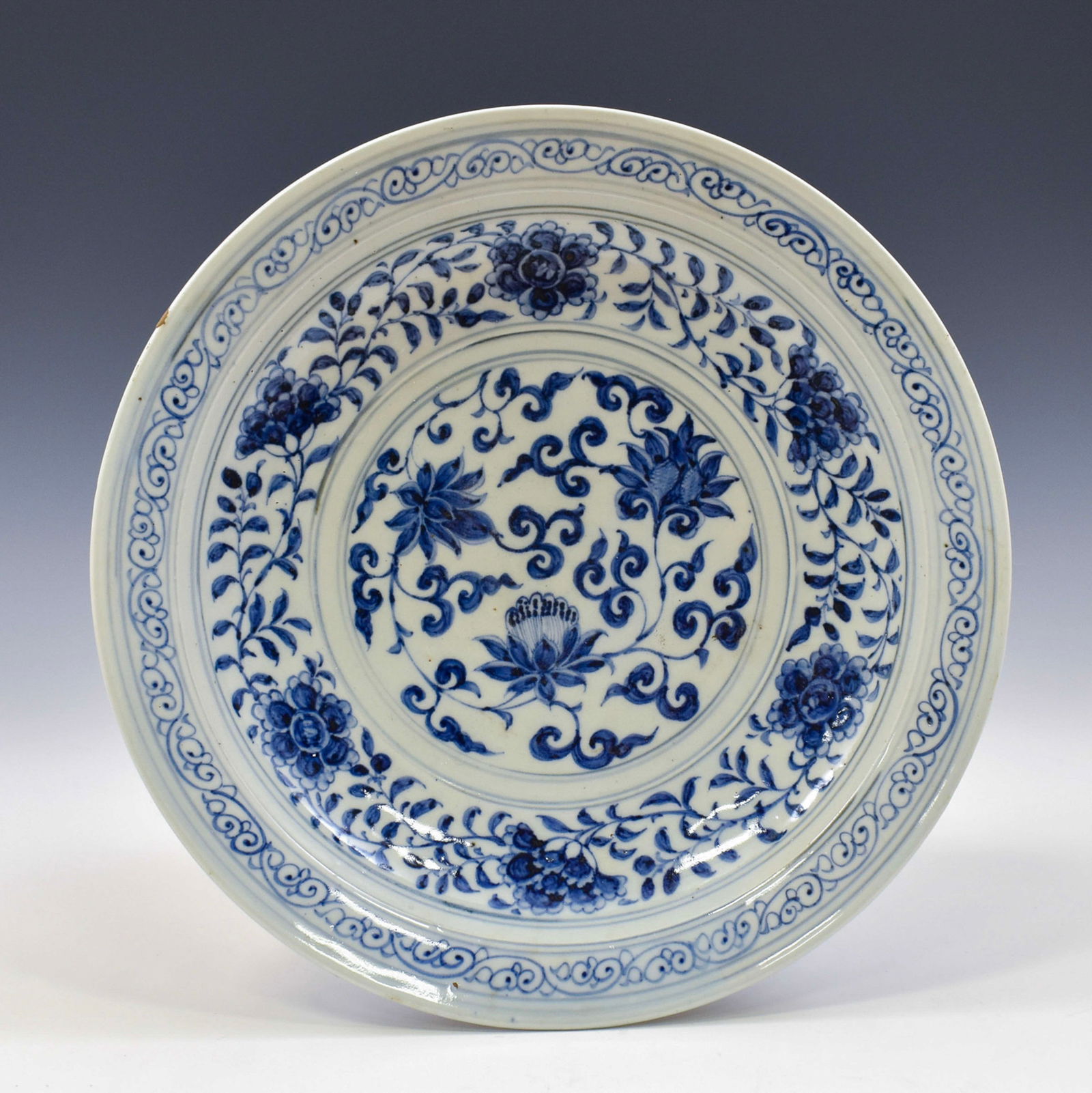 YUAN BLUE AND WHITE FLORAL PLATE: Dimensions: 11.5"L x 2.25"H Chinese Yuan Dynasty Period, blue and white floral motif porcelain plate. The porcelain potted in shallow vessel form, thick and large, with broad wide central interior, ro