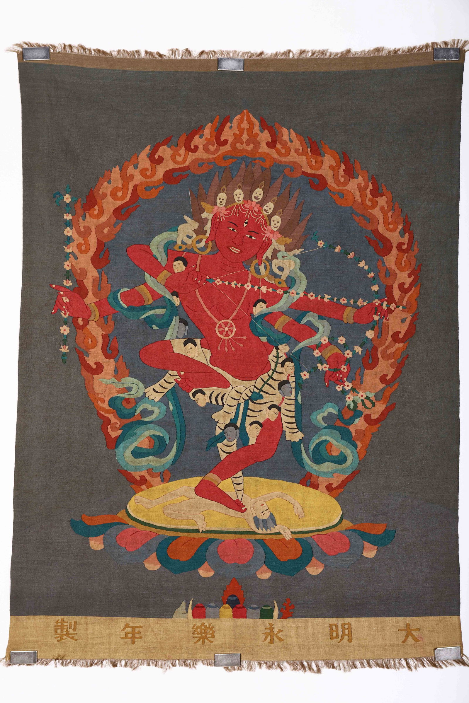 CHINESE KESI SILK DEITY THANGKA: Dimensions: L. 92 cm. W. 65 cm. This striking Chinese kesi (tapestry) silk thangka depicts a multi-armed wrathful Buddhist deity in vivid red tones, standing atop a lotus base within a flaming mandorl