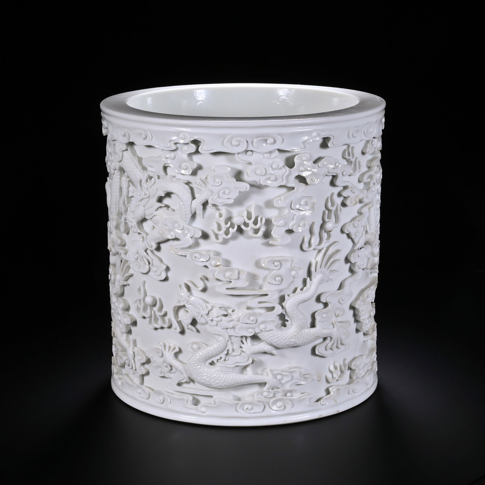A CHINESE WHITE PORCELAIN BRUSH POT WITH DRAGON DESIGN: Dimensions: H. 19.7 cm. W. 19.2 cm. This is a magnificent Chinese white porcelain brush pot, standing at 19.7 cm tall with a width of 19.2 cm. Exquisitely crafted, it features intricate bas-relief car