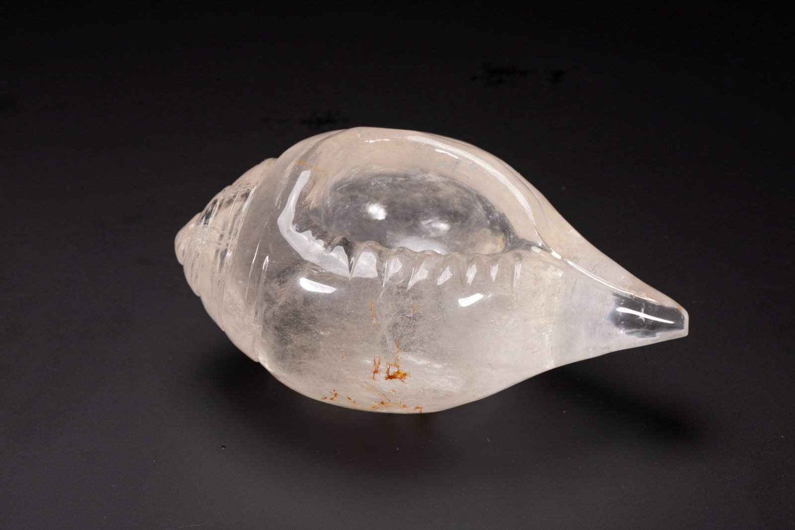A CHINESE ROCK CRYSTAL CONCH SHELL: Dimensions: L. 13 cm. W. 7.5 cm. H. 6 cm. Weight 560 grams. This exceptional Chinese ritual object is masterfully carved from a single block of clear rock crystal, meticulously shaped into the form of