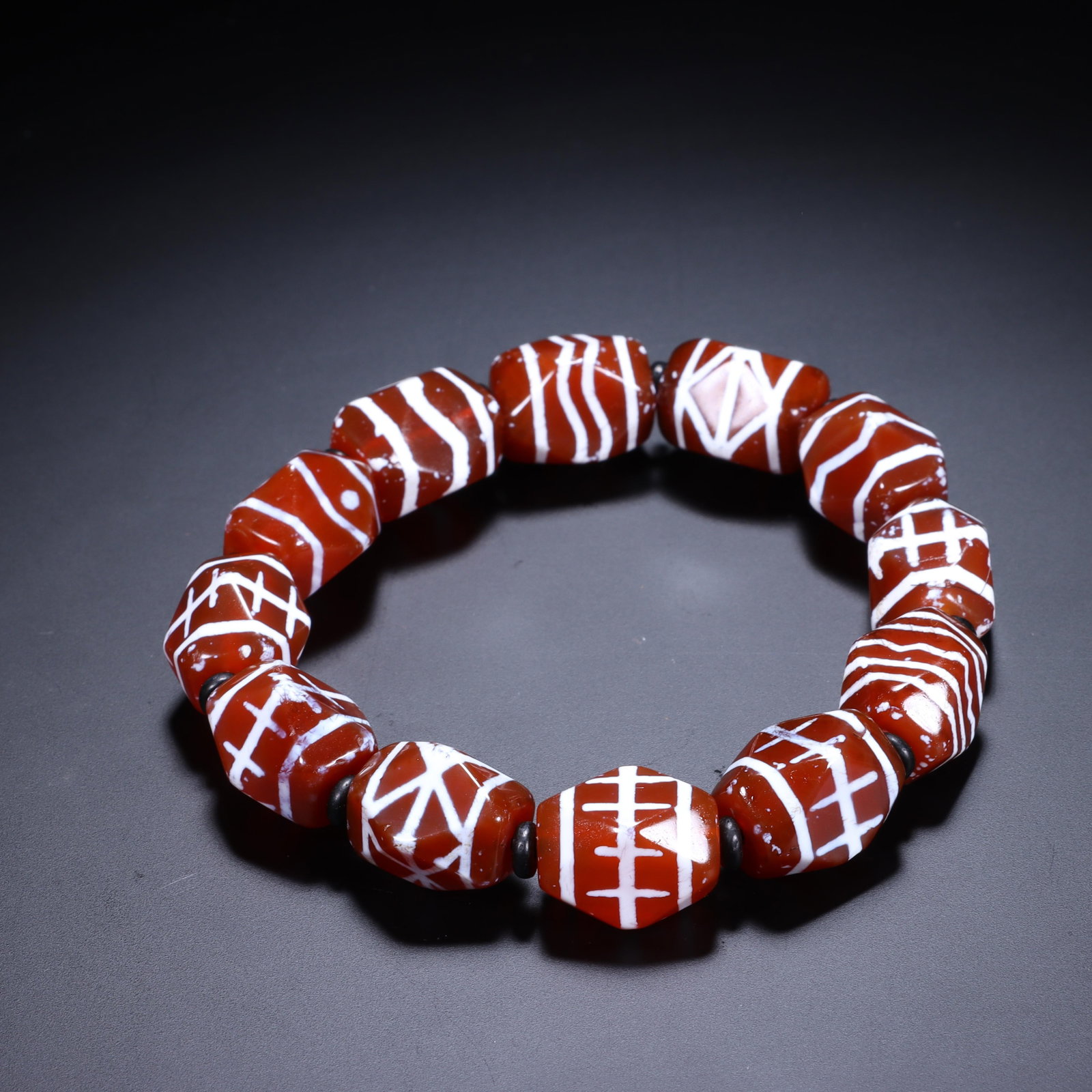 A CHINESE CARNELIAN DZI BEAD BRACELET: Dimensions: Bead diam. 1.2 cm. This striking Chinese bracelet is composed of 14 polished barrel-shaped carnelian agate dzi beads, each adorned with intricate white incised geometric and symbolic motif