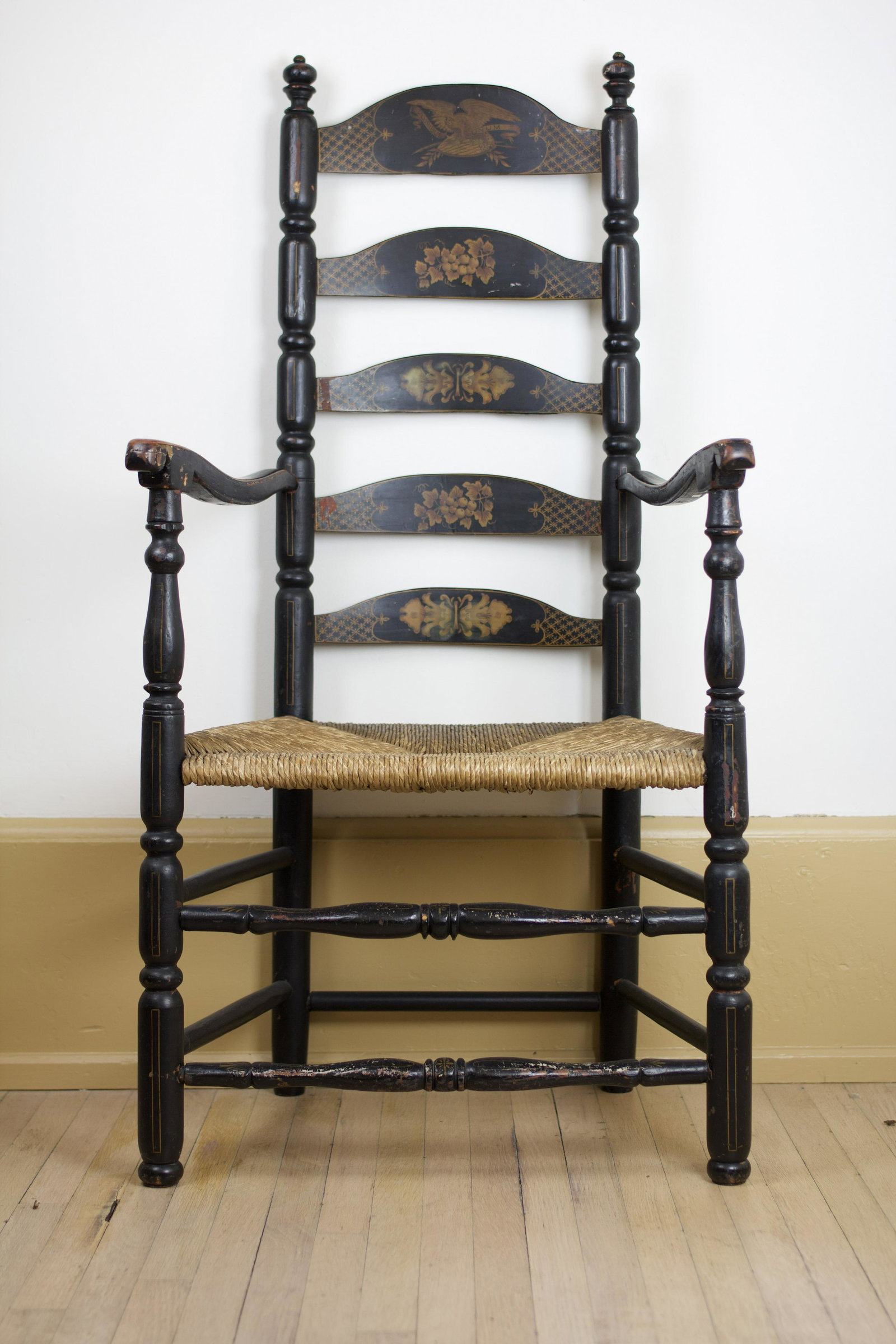 TALL DECORATED LADDERBACK ARMCHAIR.: American, 18th Century. Five graduated arched slat back rails. Wonderful decoration that is early to mid 19th Century. Top slat has an American bald eagle on a shield and olive branches. Eagle has a b