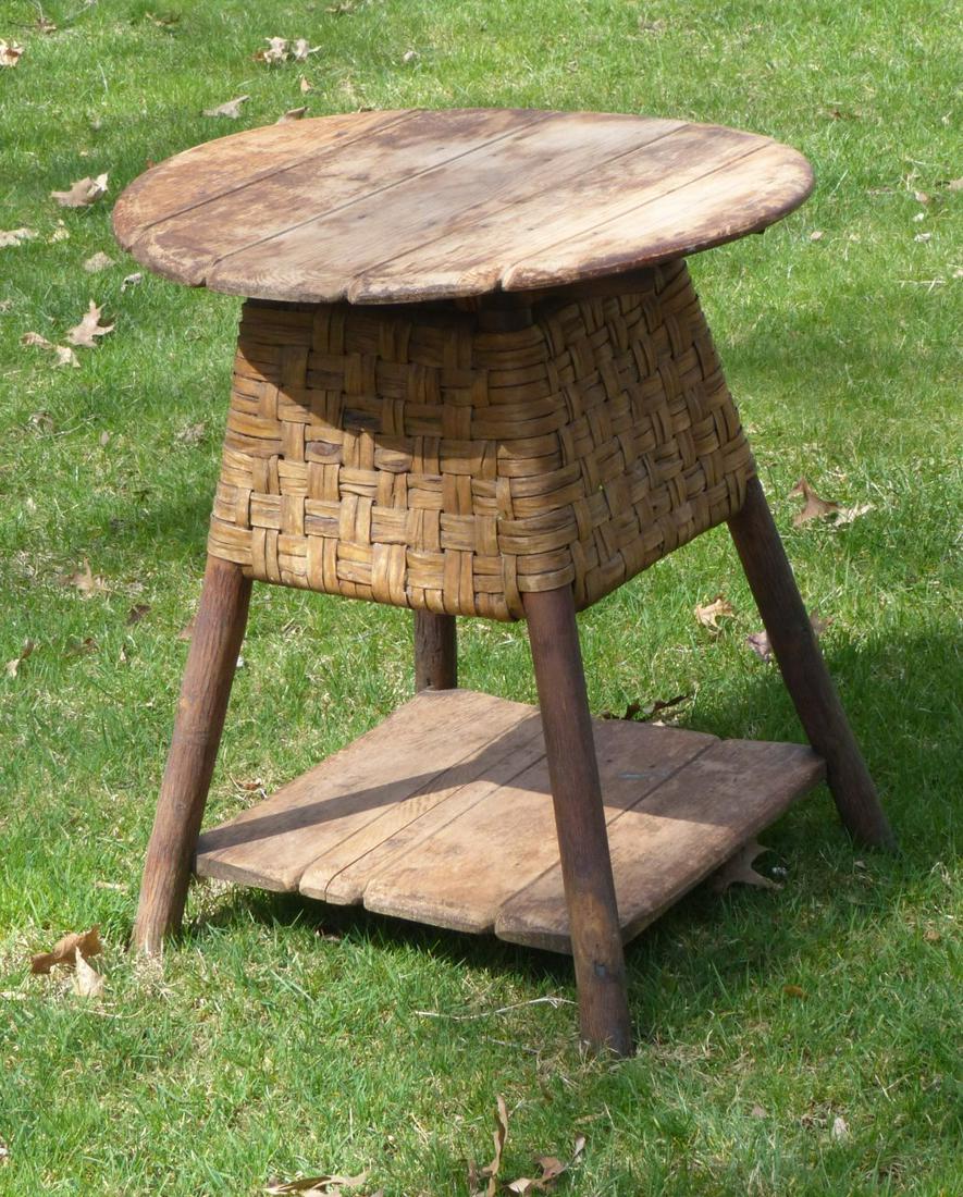 ROUND PRIMITIVE TABLE BY OLD HICKORY (SIGNED).: American (Indiana), 20th Century. Five-board top with 4 natural log legs, plank shelf underneath, wicker section at the top of the legs, stamped "Old Hickory Martinsville Indiana". 28"h. 25"d. The tab