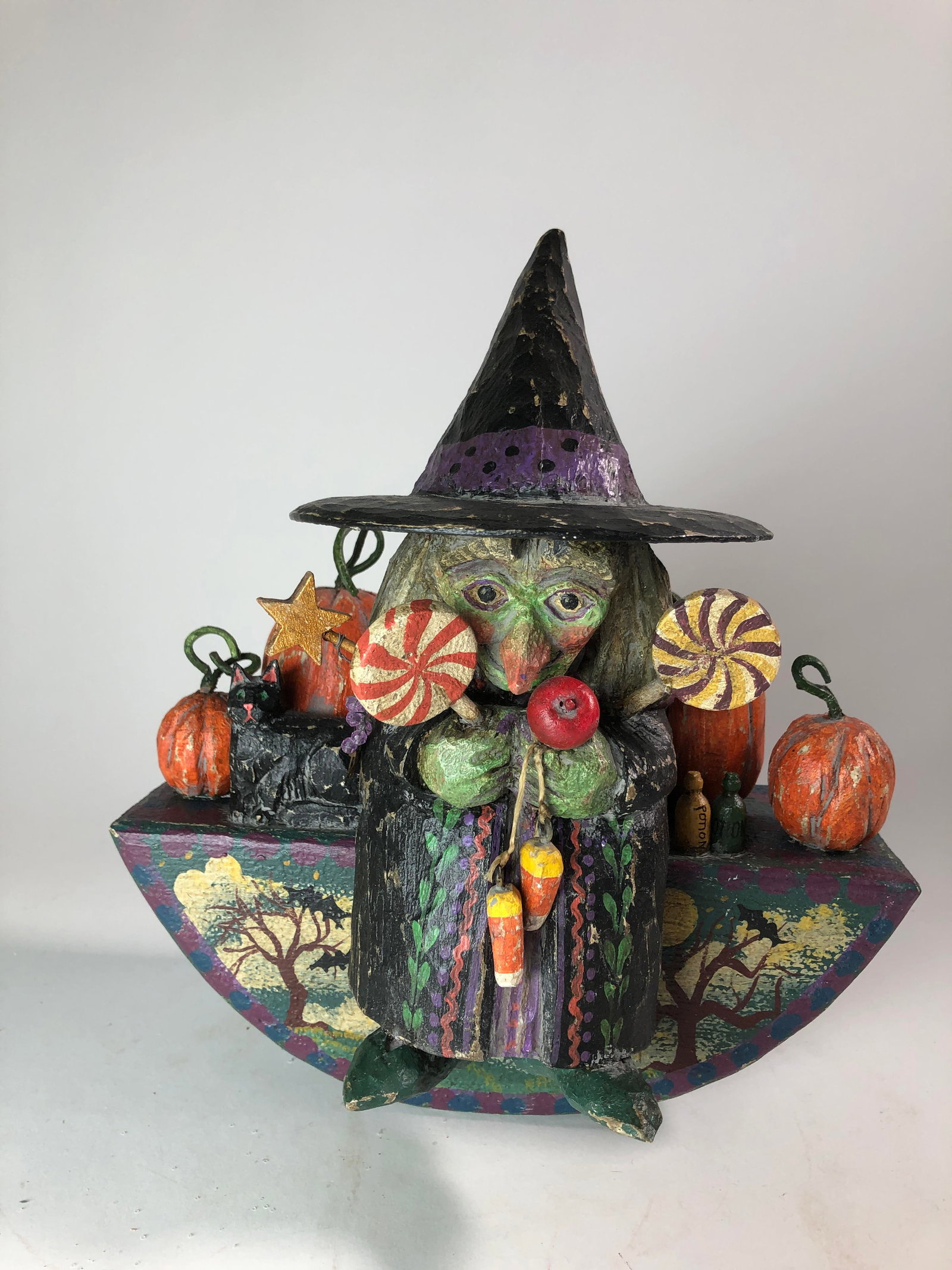 CARVED AND PAINTED FOLK ART HALLOWEEN FIGURE BY P. "PAM" SCHIFFERL.: CARVED AND PAINTED FOLK ART HALLOWEEN FIGURE BY P. "PAM" SCHIFFERL. American (Wisconsin), 20th - 21st Century. Wood, paint, and textile. A happy witch holding candy and sitting on a rocking pedestal a