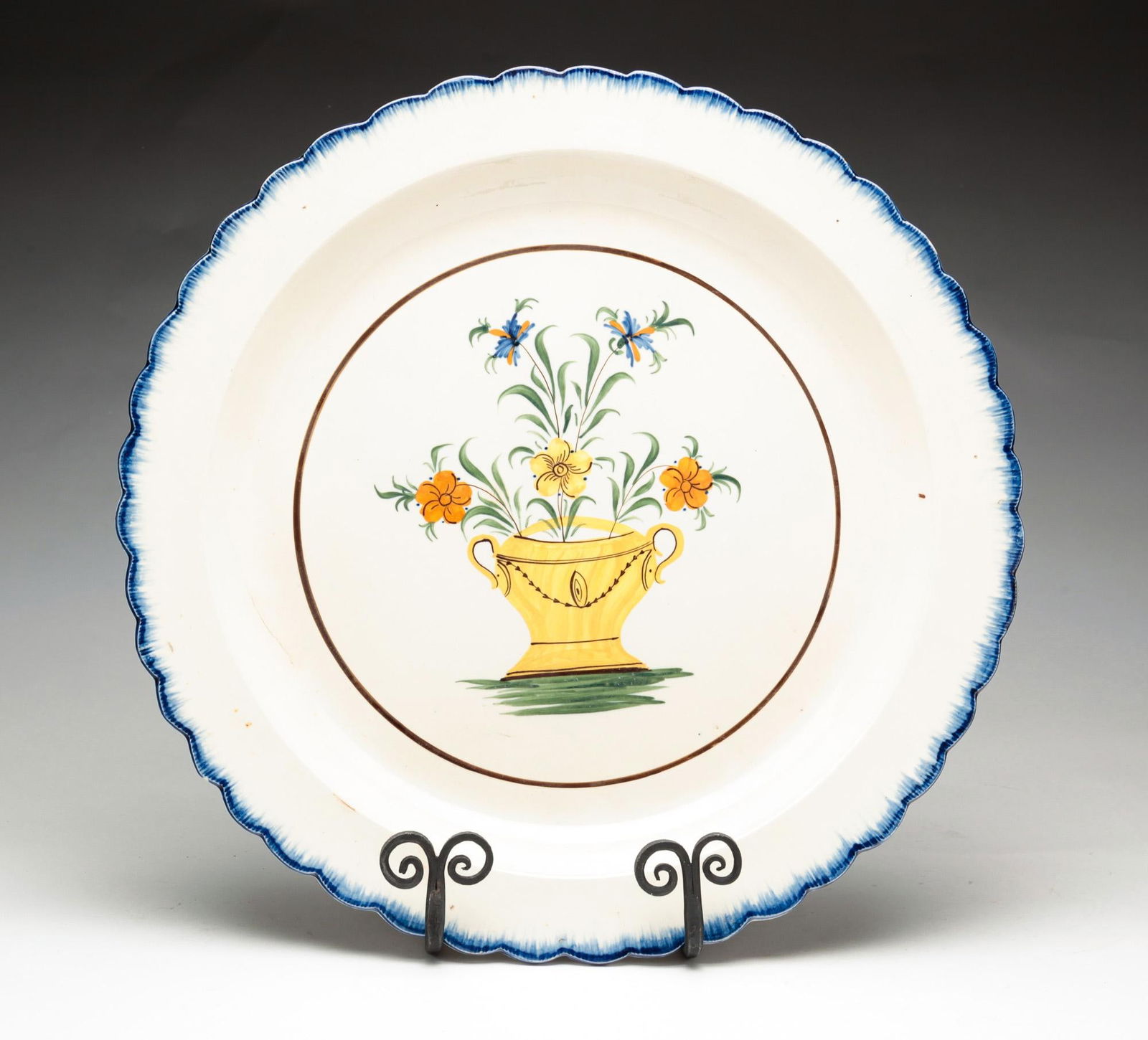 LEEDSWARE FEATHER EDGE CHARGER.: English, early 19th Century. Scalloped rim with polychrome urn of flowers in center reserve. Some discoloration, knife marks, and firing crack. 14.5"dia.