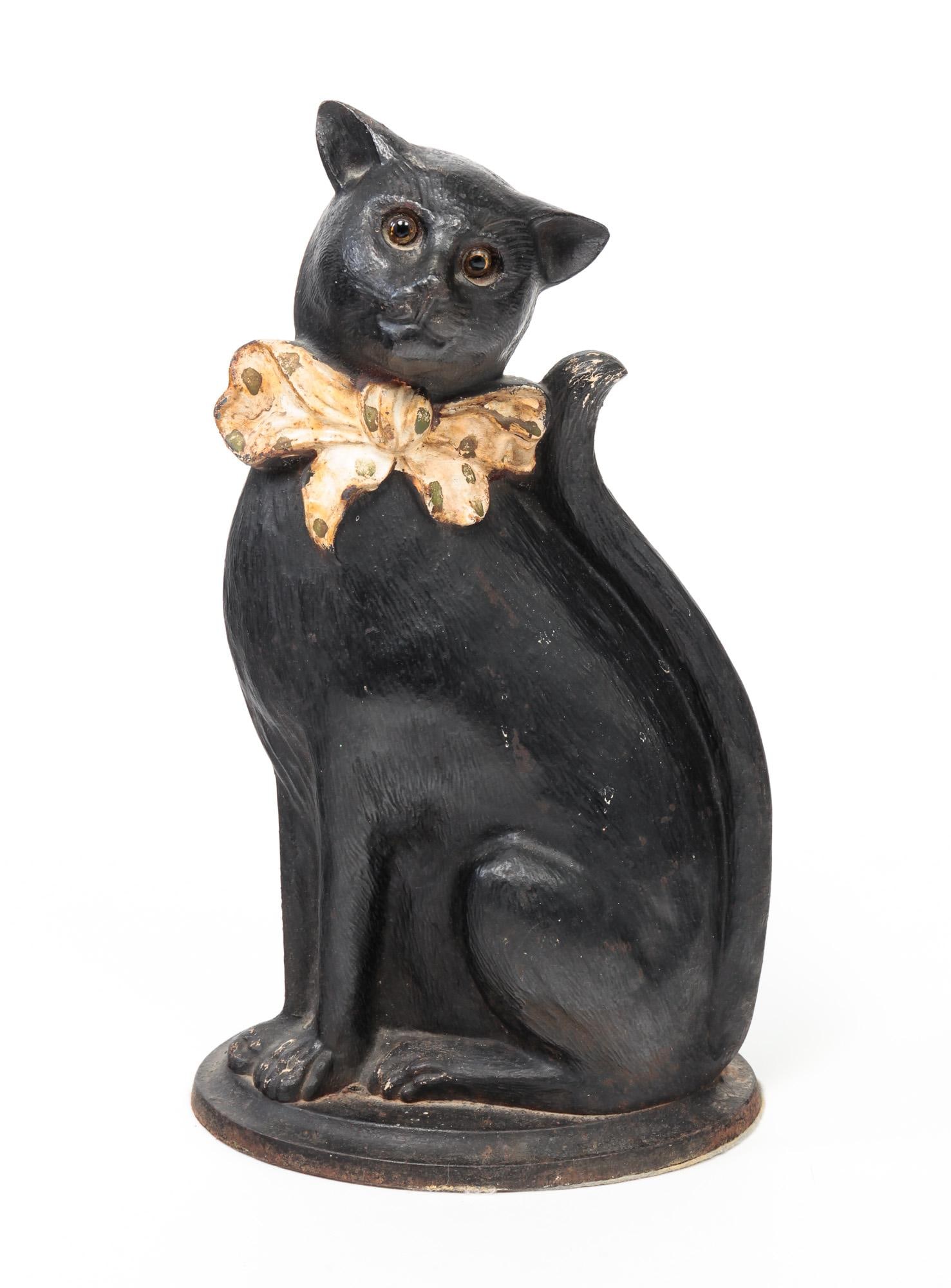 CAT DOORSTOP.: English, second quarter 20th Century. Cast iron. Black repaint over white, white neck bow with green spots, and glass eyes. Missing three hooks on back. 15"h.