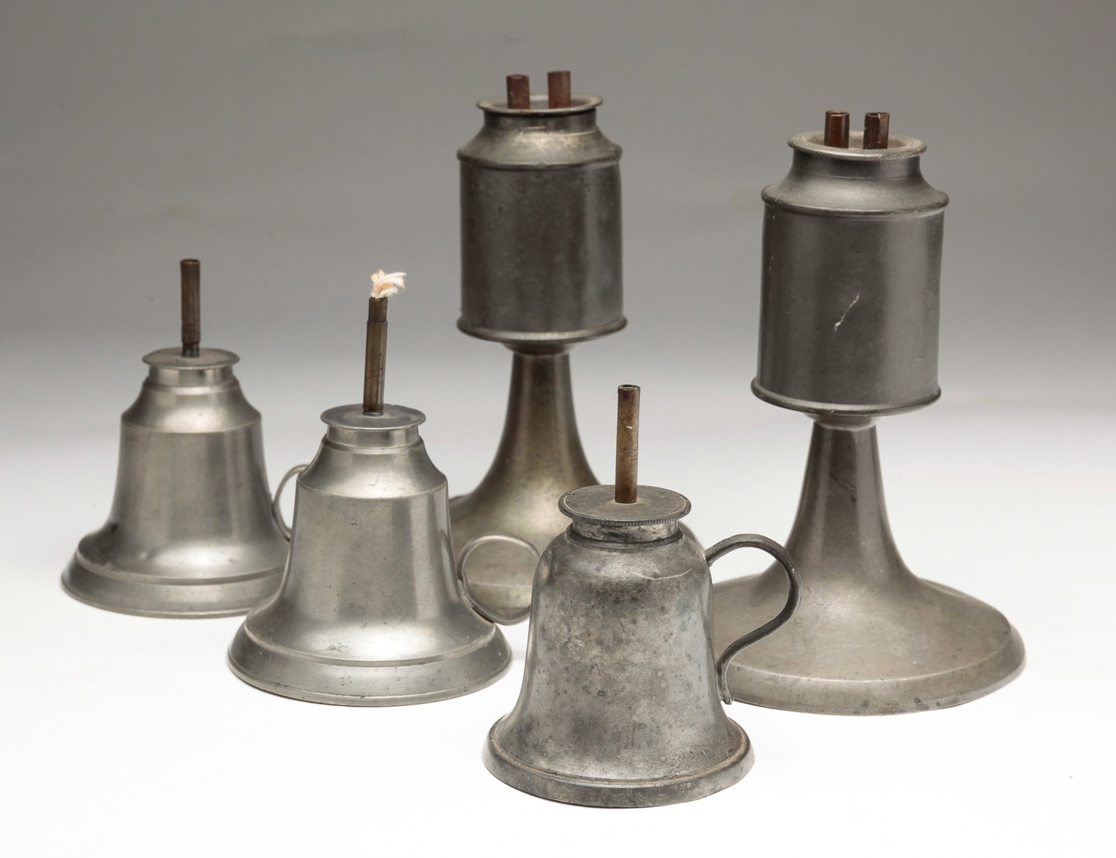 FIVE PEWTER WHALE OIL LAMPS.: American, first half 19th Century. A footed pair with double burners. 6"h, a bell shaped pair of finger lamps with single burners. Possibly Capon and Malinook, New York. 3.5"h and an unmarked bell sha