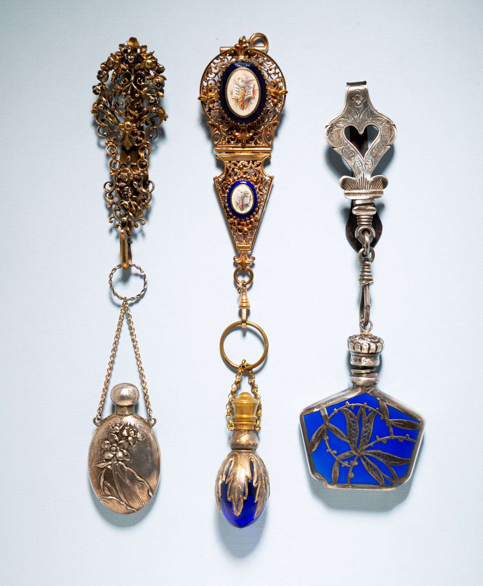 THREE VICTORIAN CHATELAINES WITH SCENT BOTTLES.: American/French, 19th Century. One silver scent bottle with hallmarks and cobalt enamel decoration suspended from bright work belt clip with French hallmark. 6.5"l. Filigree chatelaine with oval scent