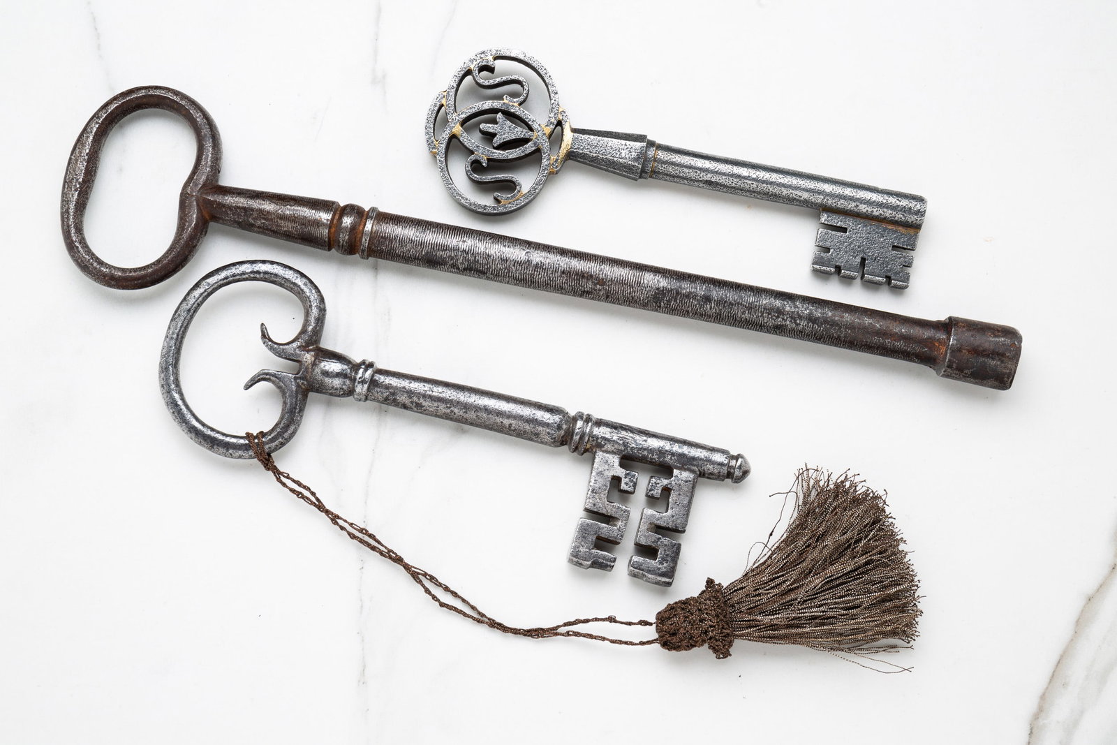 THREE LARGE ANTIQUE KEYS.: Eurpean, 19th century, iron. Two with ornate bits and bows. 6.25"-11.75"l.