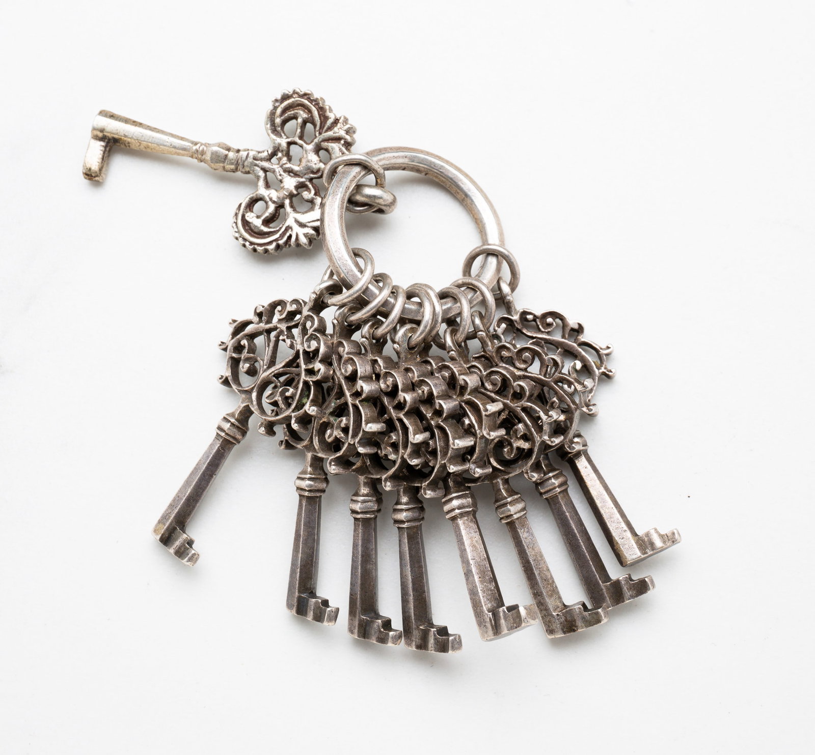 NINE SMALL ORNATE KEYS.: European, 18th-19th Century, iron. Eight matching keys and one similar key. All with elaborate scrollwork on the bow. All on one ring. 1.5"l.