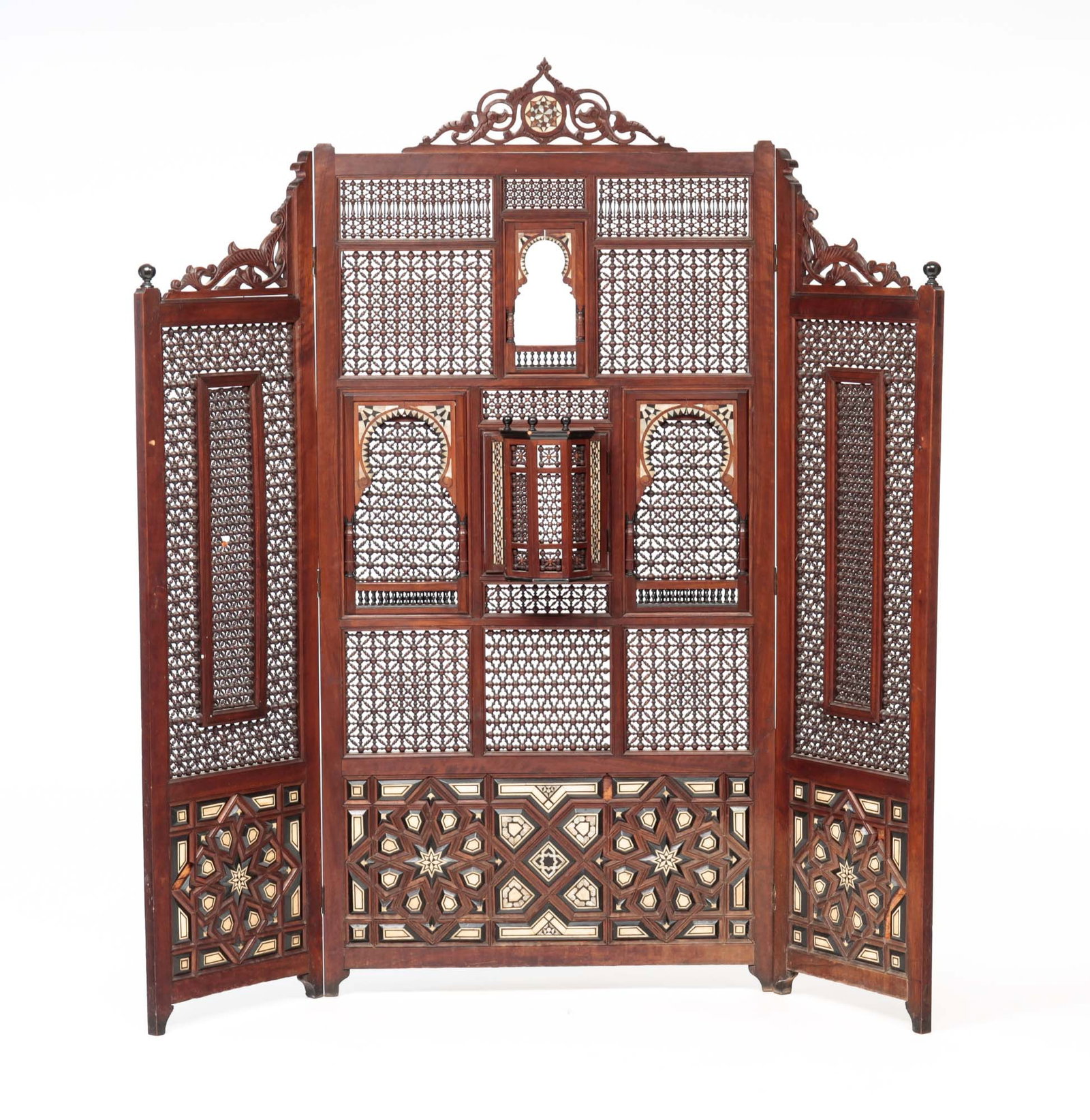 INLAID MOROCCAN FLOOR SCREEN.: First quarter 20th century, mahogany. Three panel stick and ball screen with carved crest and inlaid designs in mother of pearl, ebonized wood and bone. Center piece has four hinged panels including c