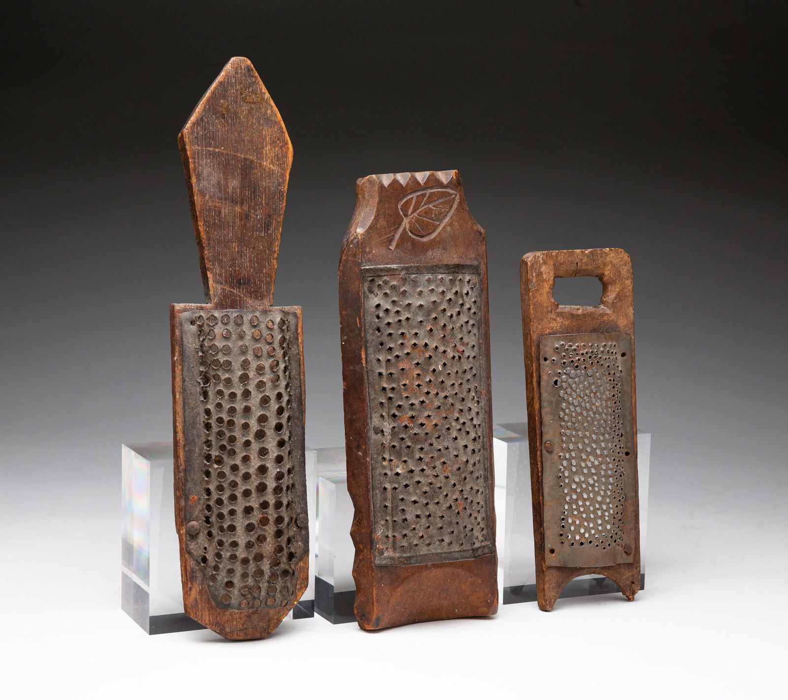 THREE SCARCE COUNTRY PIERCED TIN NUTMEG GRATERS.: American, 1800-1860. Tin and wood collection of three graters with one carved with leaf, one washboard-style, and one with a paddle handle. The largest,10".