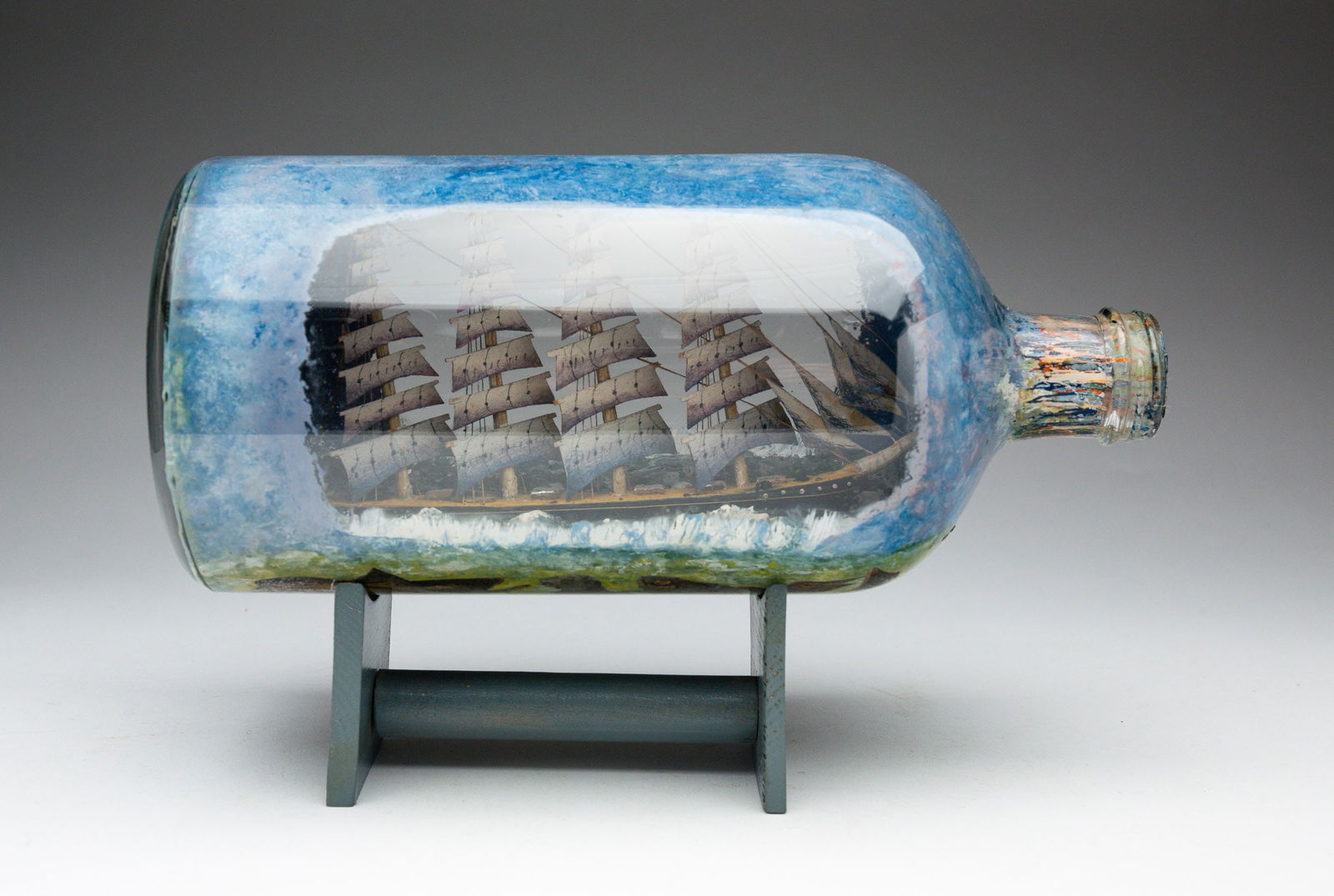 SHIP IN A BOTTLE WHIMSY WITH FISH.: American or English, circa 1880. Wood and tin ship in a bottle whimsy on the obverse; with decoupage fish on the rear. Label that reads "Pirate Ship" on the bottom of bottle. Overall, 10"l.