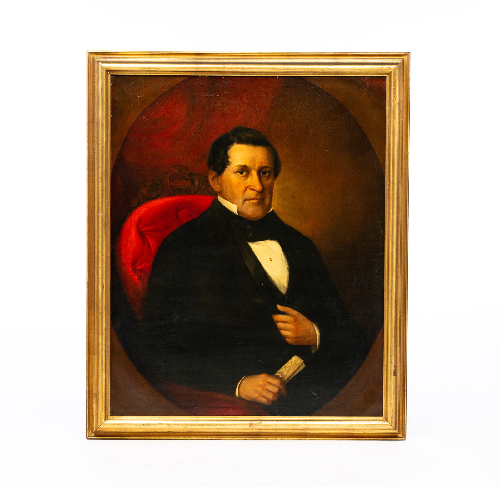 PORTRAIT OF A GENTLEMAN.: American, Mid 19th Century. Oil on canvas. He wears a black tie, coat and vest, holds a rolled document and is seated on a carved chair with tufted red upholstery. Cleaned, revarnished, crazing and so