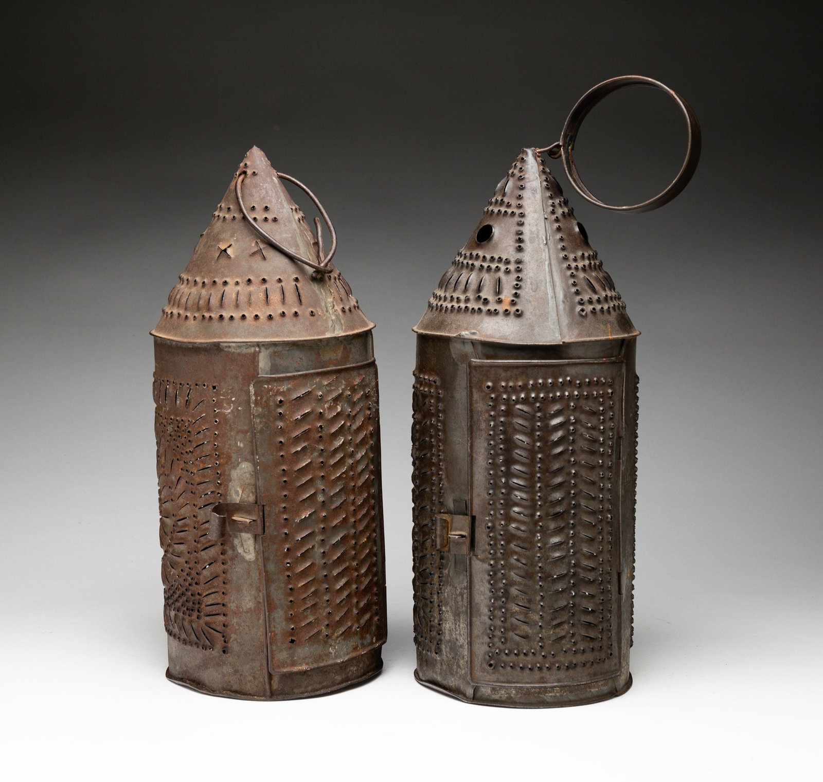 TWO PUNCHED TIN REVERE-TYPE CANDLE LANTERNS.: American, 19th Century. Two cylindrical punched tin candle lanterns with hinged doors, conical tops, and round hangers. 13"h. Overall, 16"h. with handle. From the collection of the late Audrey Caspari