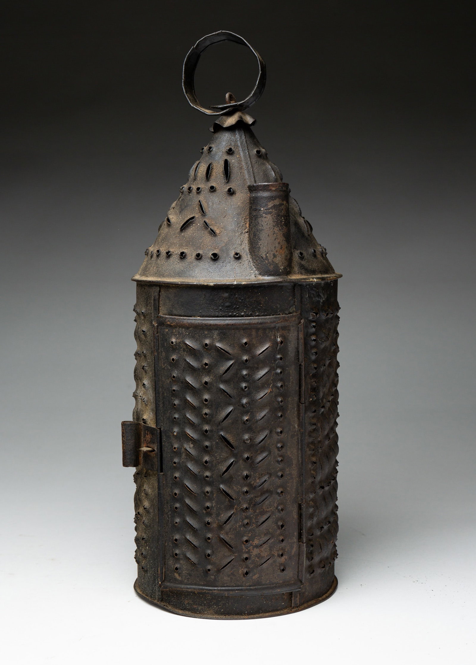 PUNCHED TIN REVERE-TYPE LANTERN WITH SMOKESTACK.: American, 19th Century. Cylindrical, punched tin candle lantern with unusual "smokestack" over hinged door. Conical top and round hanger. Overall, 15.5"h. From the collection of the late Audrey Caspar
