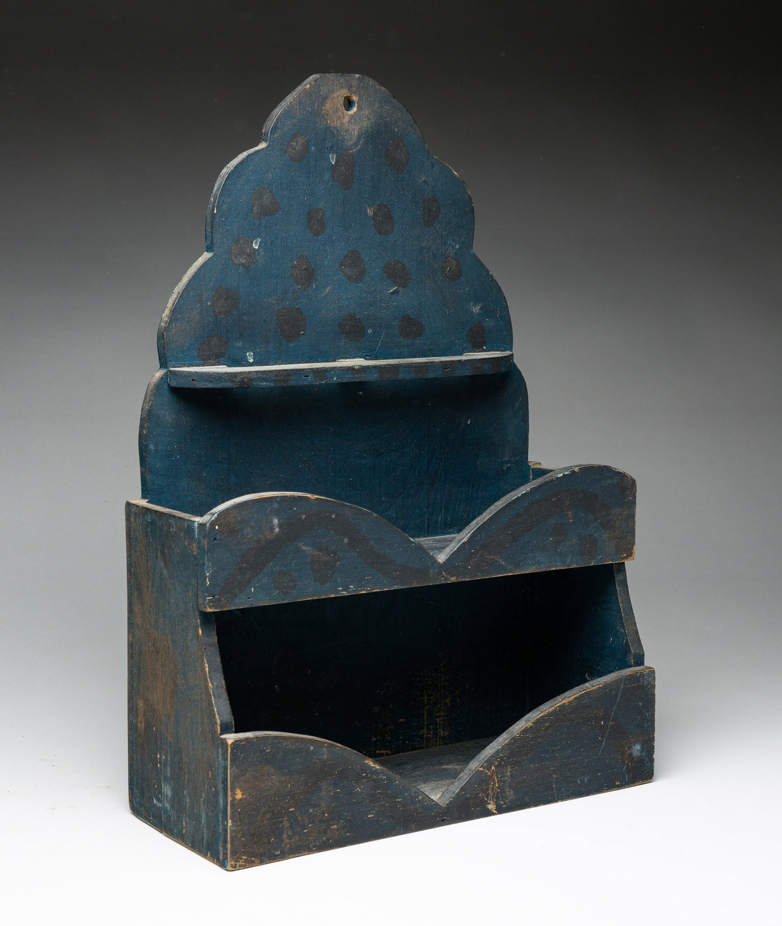 FOLKSY BLUE PAINTED WOOD WALL SHELF: American, 19th Century. Black polka dots over blue paint. Scroll-cut shaped back, spoon 16.75"h., 11.75"w., and 4.75"d. From the collection of the late Audrey Caspari (New Jersey).