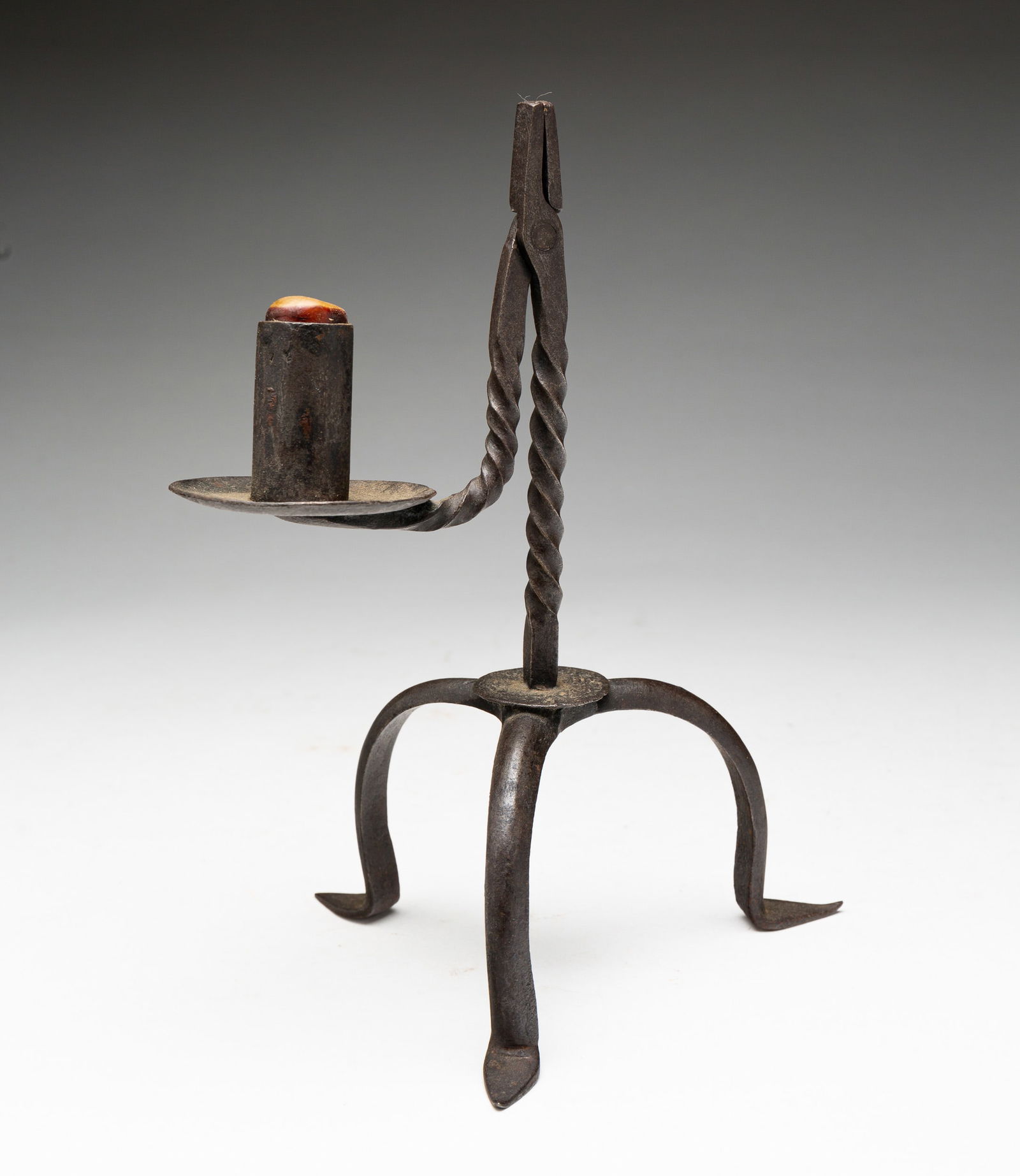 WROUGHT IRON TABLE-TOP RUSH LIGHT.: American, 18th Century. Twisted shaft supporting combination form of rushlight holder, counterweighted with a single-socket candle holder and drip pan, raised on three cabriole. Overall, 8.75"h. From
