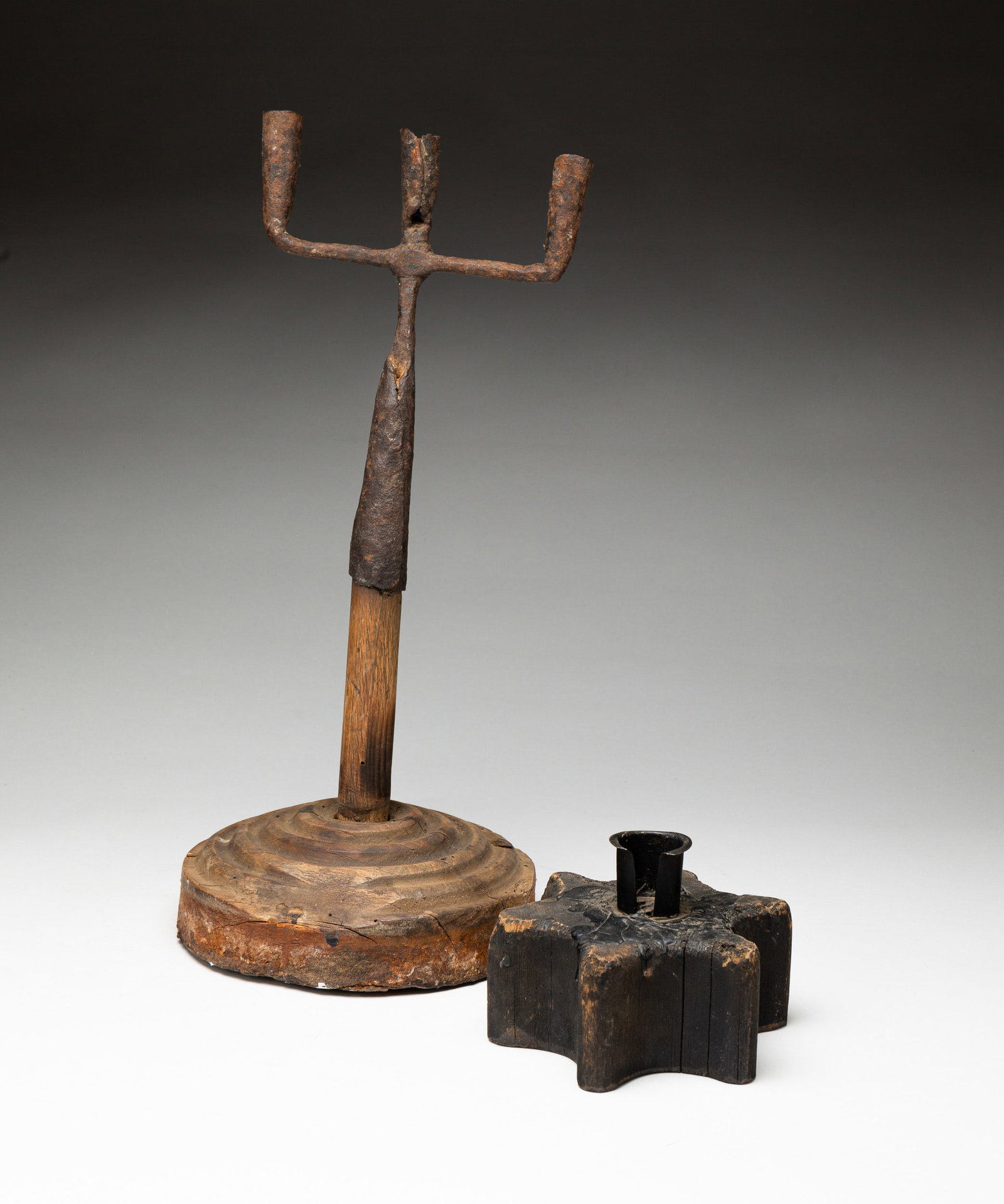 TWO MAKE-DO LIGHTING PIECES.: American, 18th Century. Iron. One candle stick and one triple candelabra on wood base. 7"h. Six-point star, 5"d. From the collection of the late Audrey Caspari (New Jersey).