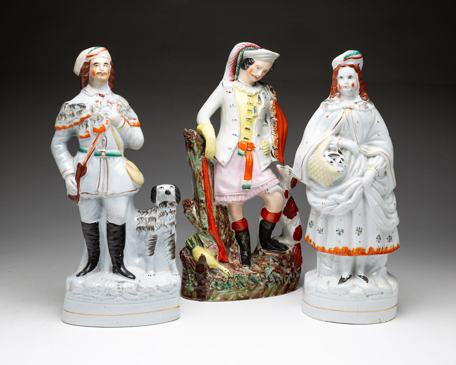 THREE STAFFORDSHIRE FIGURINES.: English, second-half 19th Century. A hunter with rifle and dog, 14"h. A lady with a rabbit in a basket, 13.75"h. A brightly colored hunter, 14.25"h.