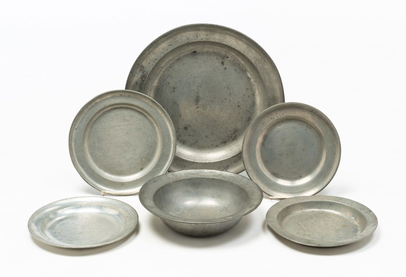GROUP OF PEWTER PLATES AND DISHES.: Continental, 19th Century. Large Neeff charger, dents and wear. 14"dia. Four plates, some partial marks, wear and loss. 8.25" - 9.25"dia. Together with one bowl. Wear. 9.75"dia.