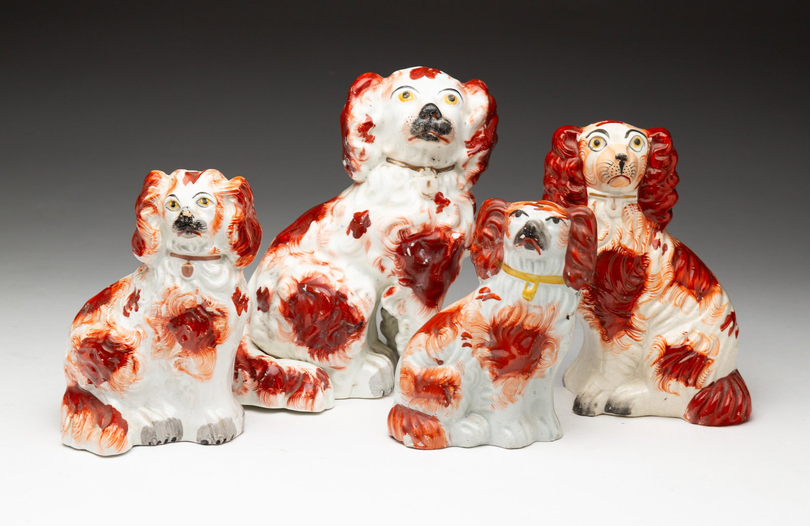 FOUR STAFFORDSHIRE SPANIEL FIGURINES.: English, second-quarter 19th Century. Graduated spaniels in rust red and white. Crazing, paint loss and minor chips. Crack in bottom of smallest. 7"h. - 4.75"h.