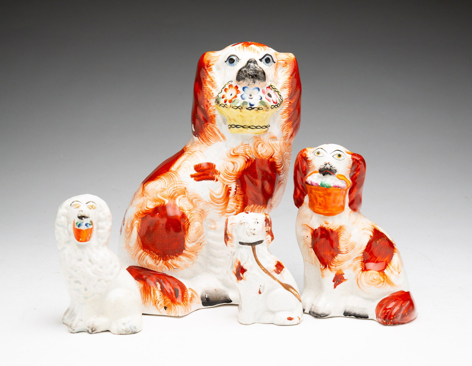 FOUR STAFFORDSHIRE SEATED SPANIELS: English, second-half 19th Century. Graduated sizes. Three largest holding baskets in mouths. 8.25"h., 5.5"h. And 4"h. Smallest with leash, 3.5"h. Paint loss and crazing throughout.