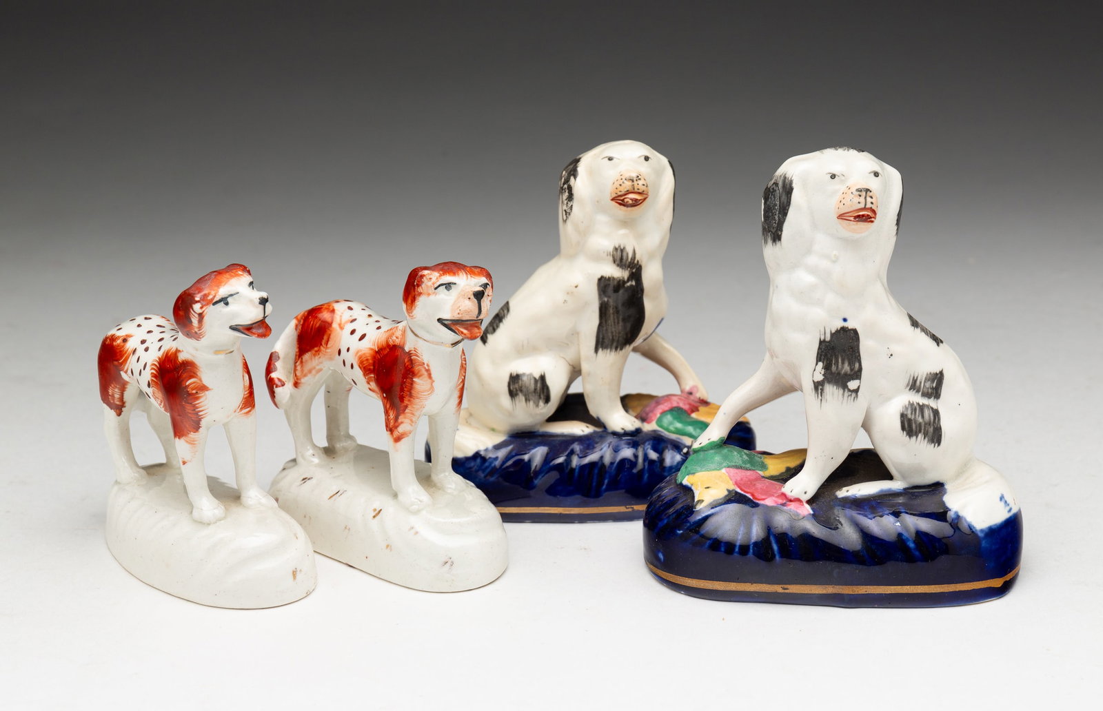 FOUR SMALL STAFFORDSHIRE DOGS.: English, second-half 19th Century. Both are male and female pairs. One pair are seated and are on cobalt bases, 4.25"h. And 4"h. The second pair are standing and have rust colored patches and spots, 3