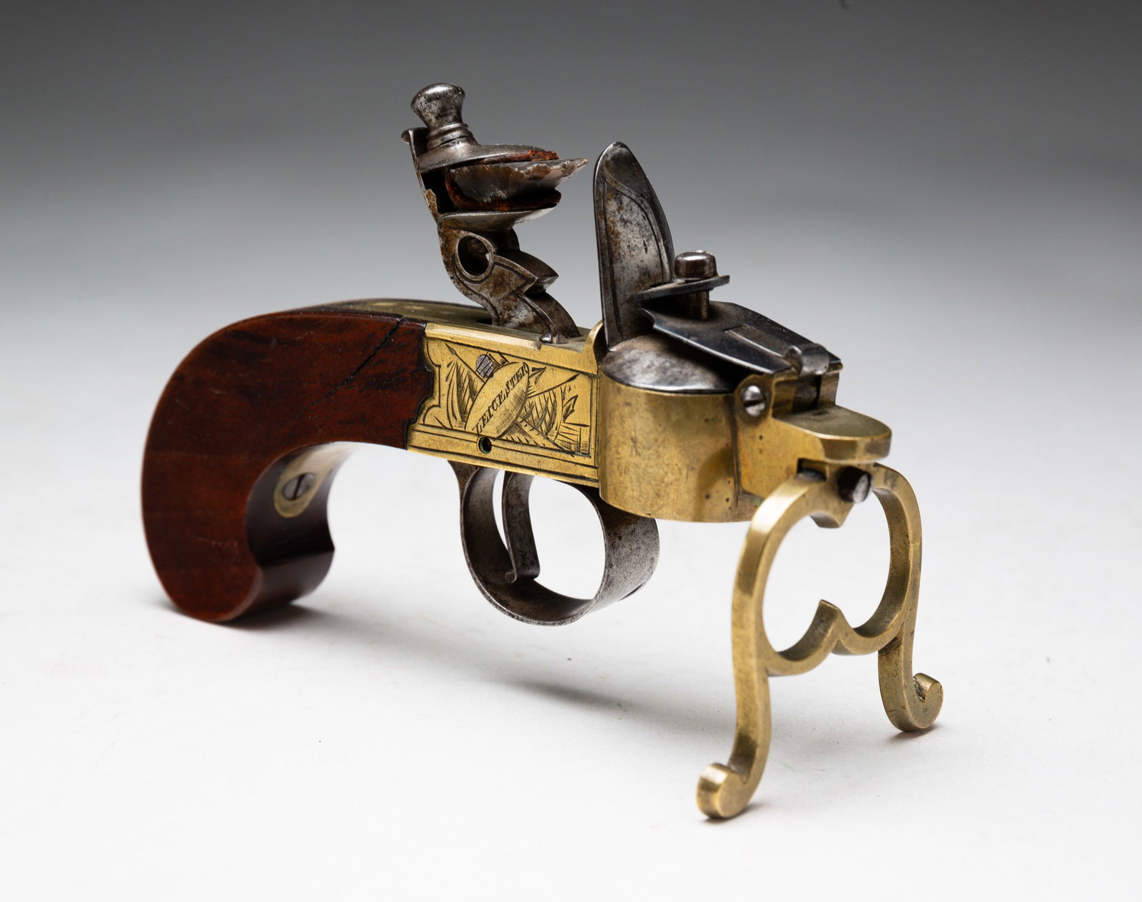 ENGRAVED FLINT LOCK PISTOL TINDER LIGHTER.: English, mid-late 18th Century. Walnut stock with brass fittings. "Leicester" and "Hind" engraved to either side. Brass stand and engraved steel trigger guard and cap. 3.75"h. 5.5"l.