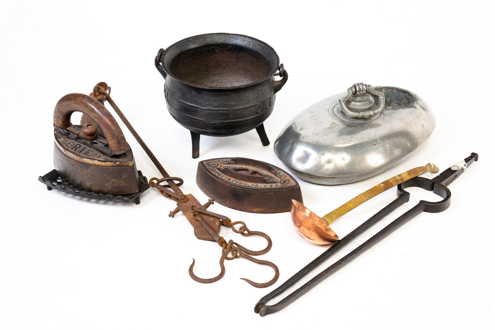 GROUPING OF HOUSEHOLD ITEMS.: American and English, mid 19th Century. Including sad irons with one trivet, pewter foot warmer, copper and brass ladle, footed half gallon cauldron, iron tongs and a scale. Varying wear and loss.
