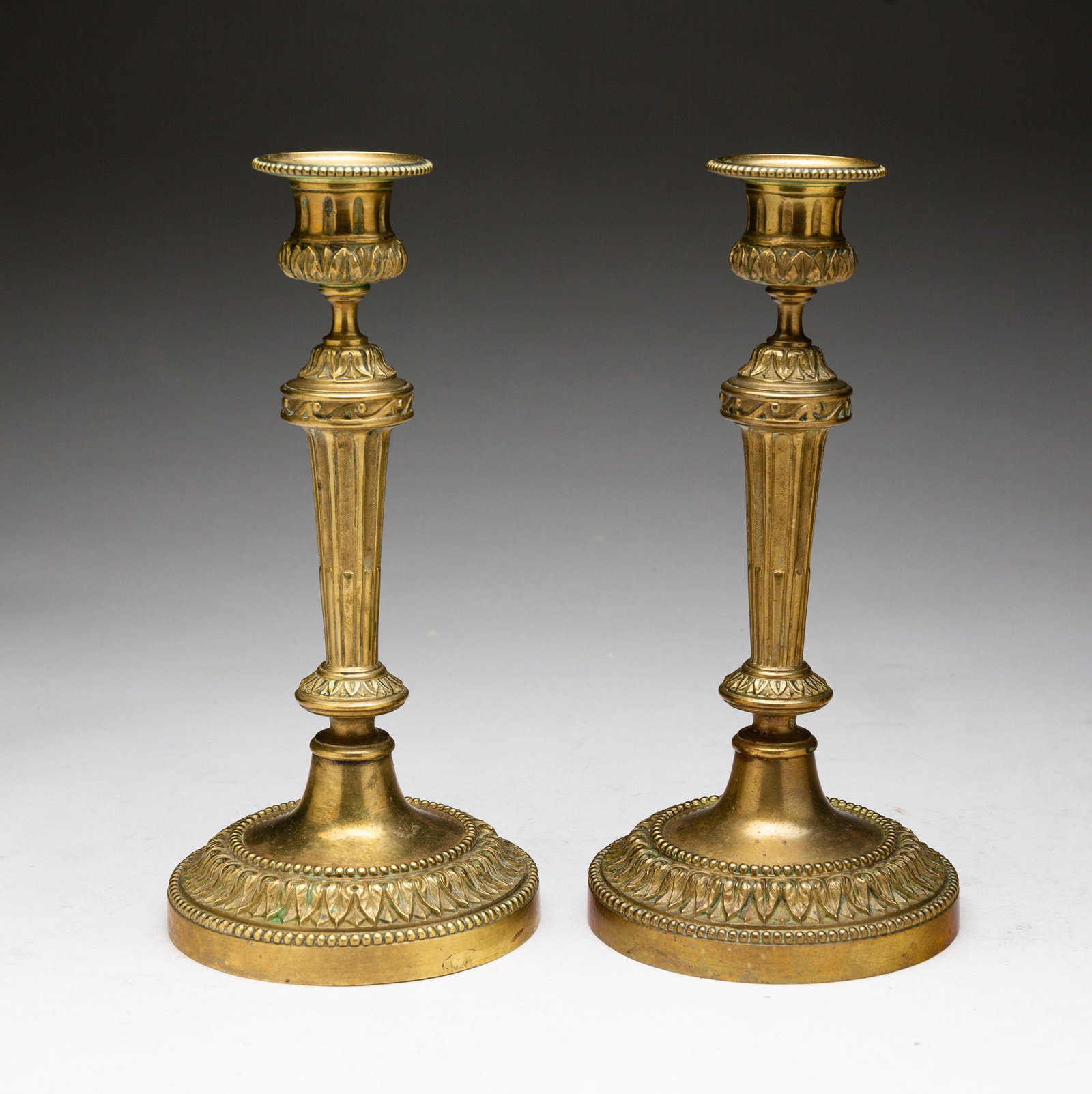 PAIR OF BRASS CANDLESTICKS.: French, 19th Century. Round bases, leaf and beaded decoration and reeded stems. Residue to cups. 9"h.