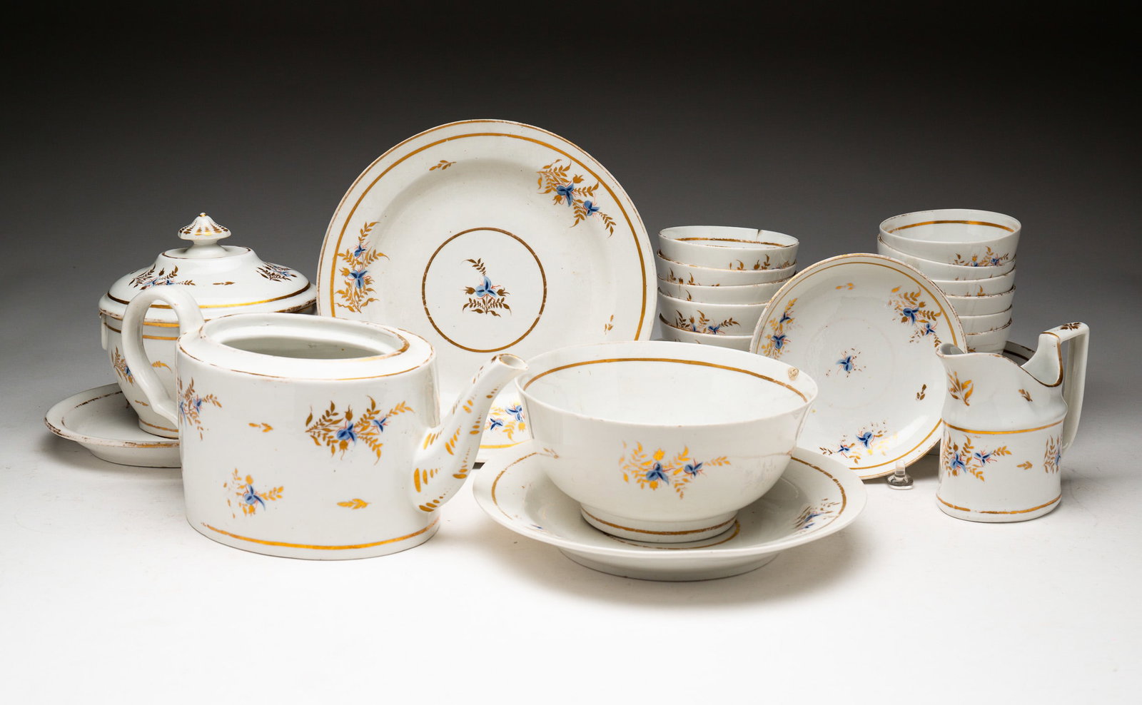 GROUPING OF PORCELAIN DISHES.: English, circa 1800. Porcelain. White ground with blue and gold floral accents. Teapot, creamer, lidded sugar, cups and saucers, teapot (no lid) and bowls. Chips, hairlines and wear.