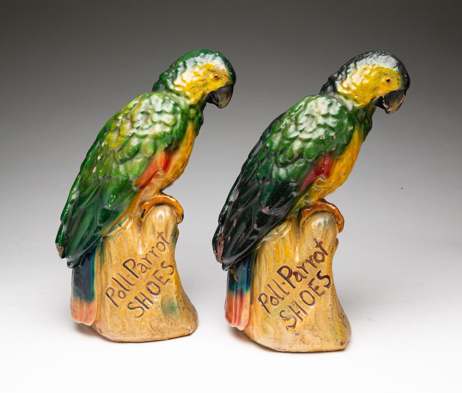 PAIR OF POLL-PARROT SHOES ADVERTISING FIGURINES.: American, second quarter 20th Century. Molded and painted plaster parrots on branch figurines. Wear to paint. 11"h.