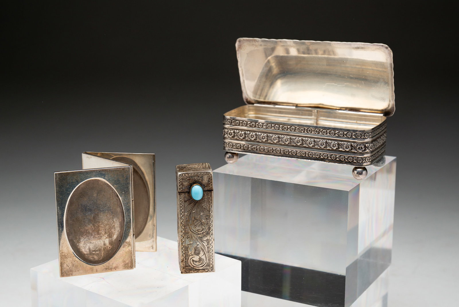 THREE STERLING PIECES.: Folding, three slot picture frame, 2.5"h.; engraved lipstick with mirror, 2.25"l.; and a footed box, monogrammed, 1"h. 3.5"w. One foot on box is corroded. Approximately 3.5ozt.