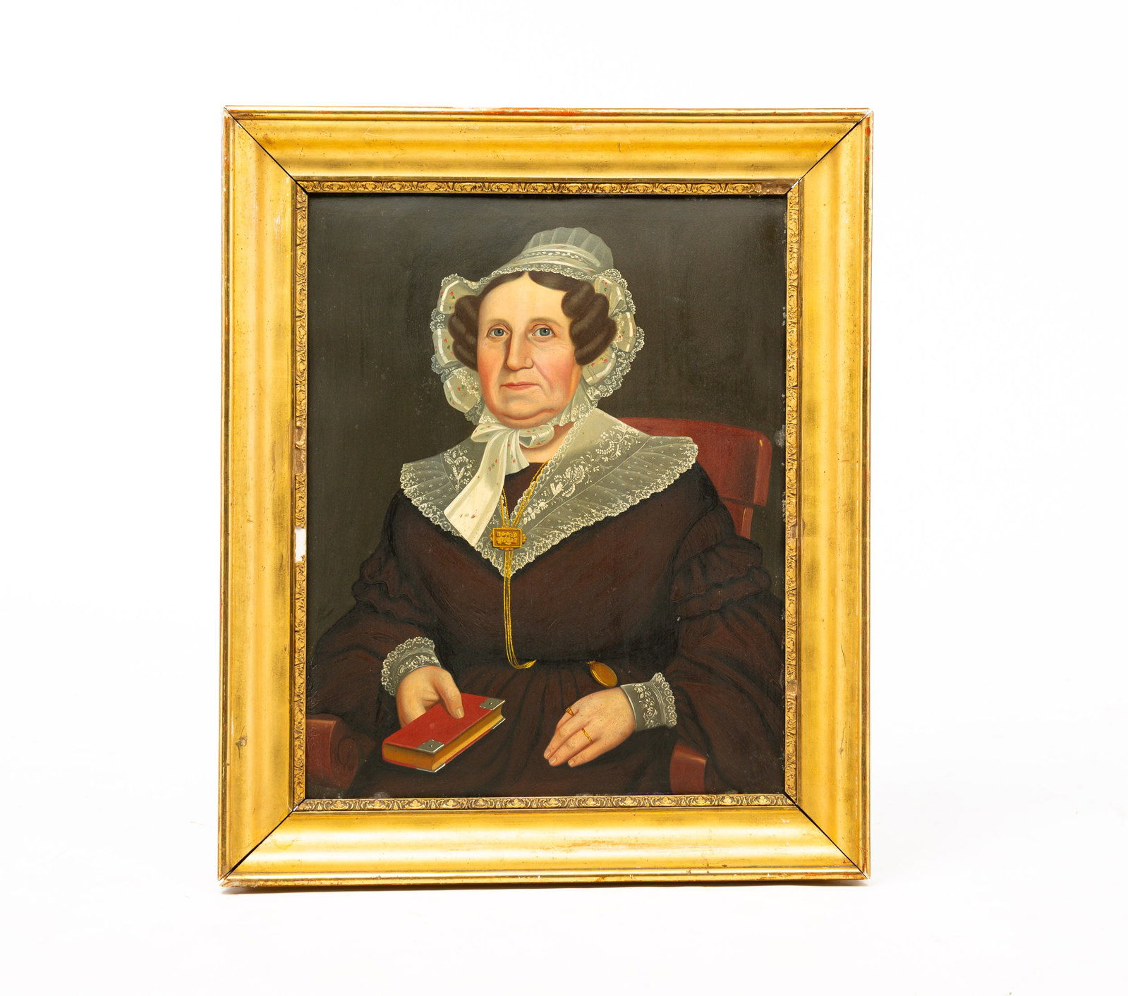 UNKNOWN ARTIST "PORTRAIT OF AN ELDERLY LADY".: American, mid 19th Century. Oil on tin. She wears a brown dress, a lace bonnet, collar and cuffs and a watch chair with elaborate slide and holds a red covered book. Nice condition with some wear arou